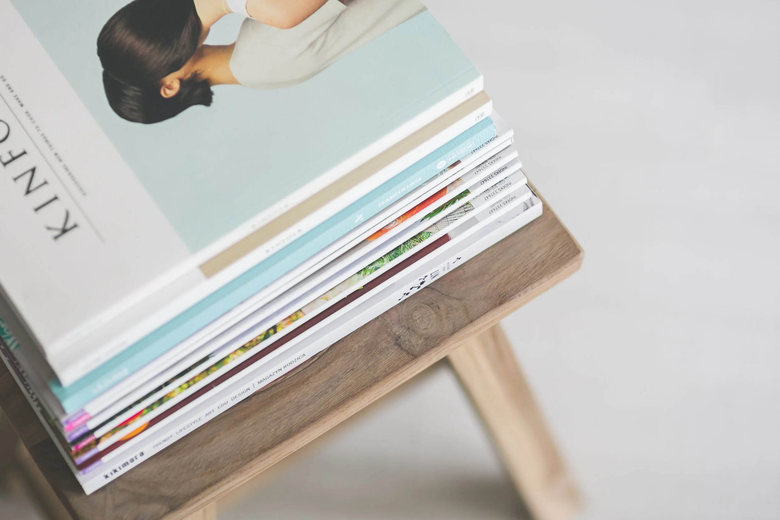 Stack of magazines or books with colorful covers on a wooden surface.