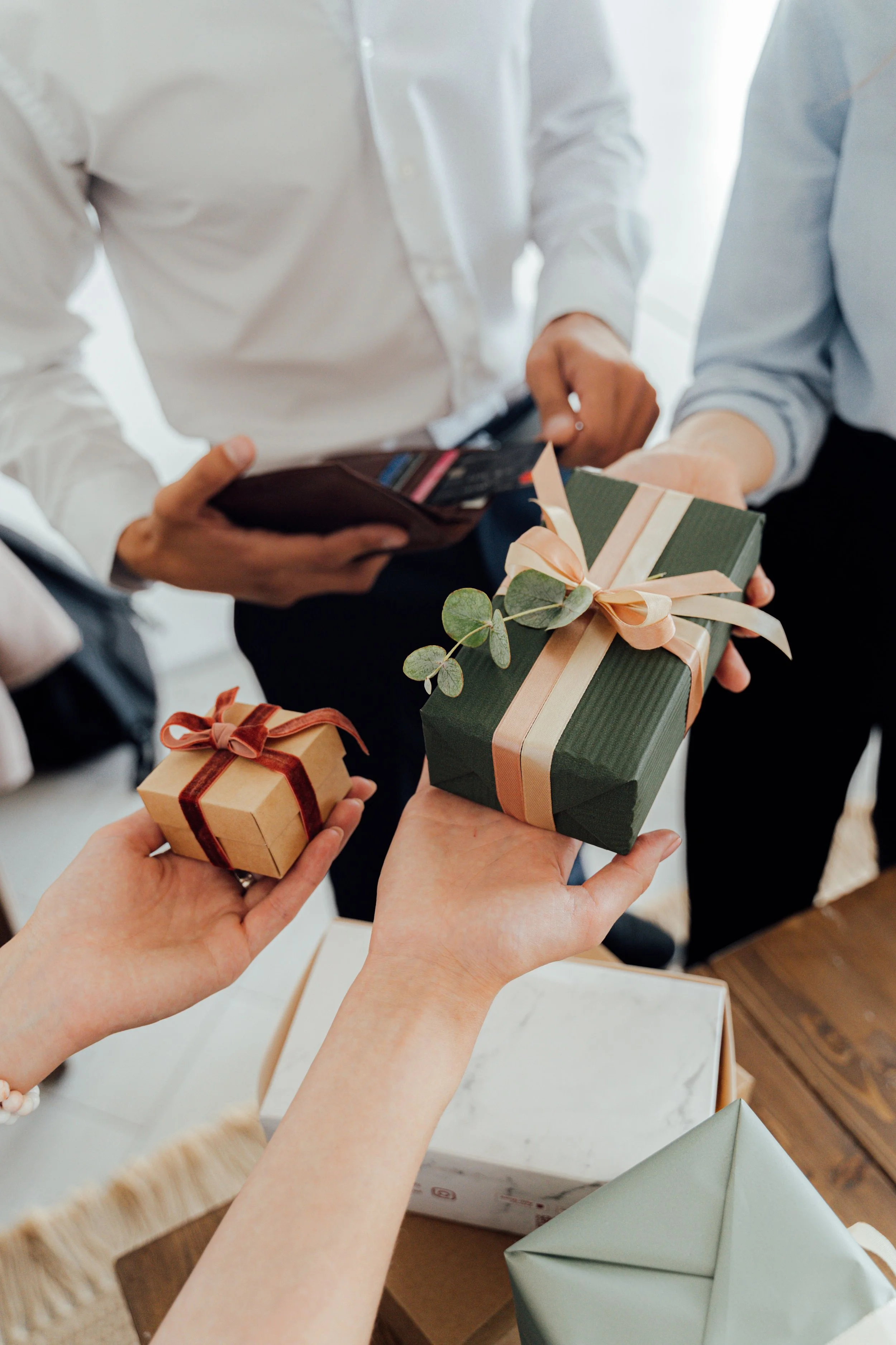 People exchanging wrapped gifts, some hands holding small boxes with ribbons, in a festive setting.