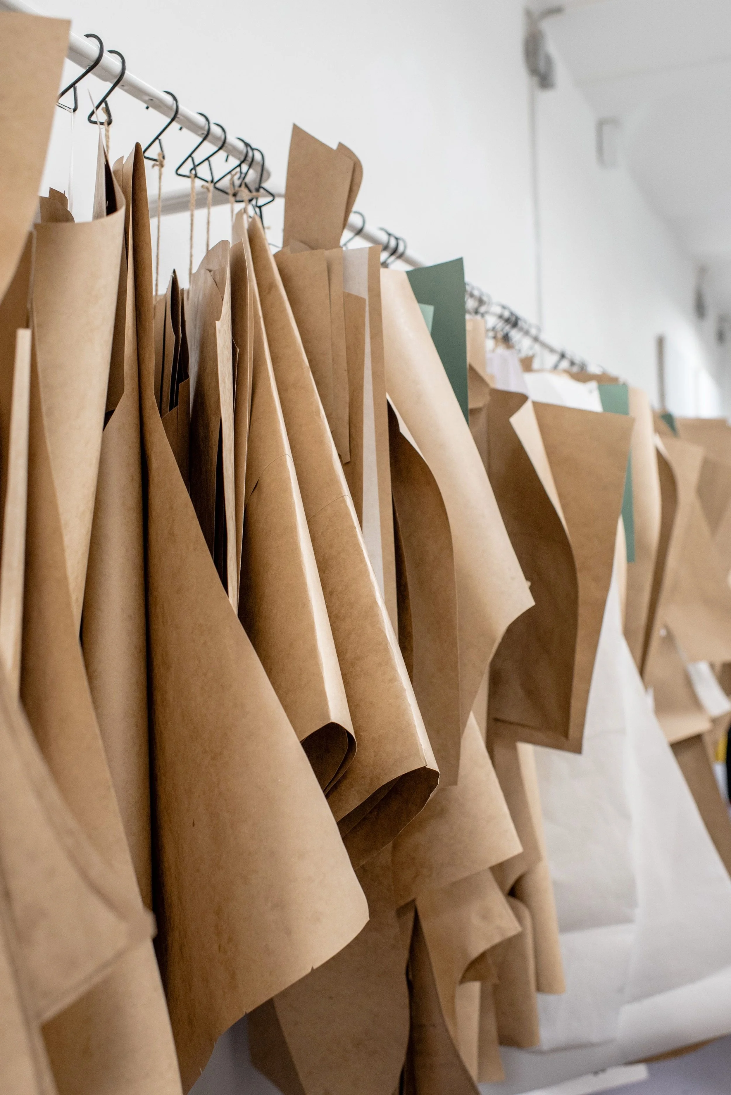 Row of brown paper bags hanging on a metal rod in a workshop or storage room.