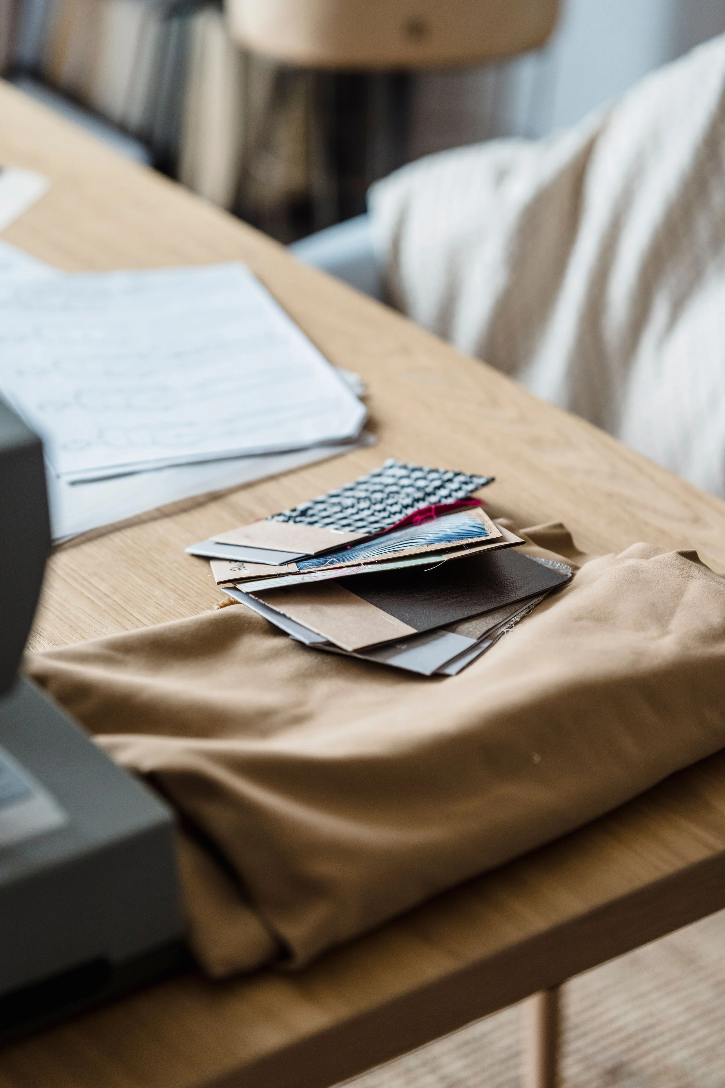 A stack of fabric swatches and sample booklets on a wooden table next to a beige fabric bag.