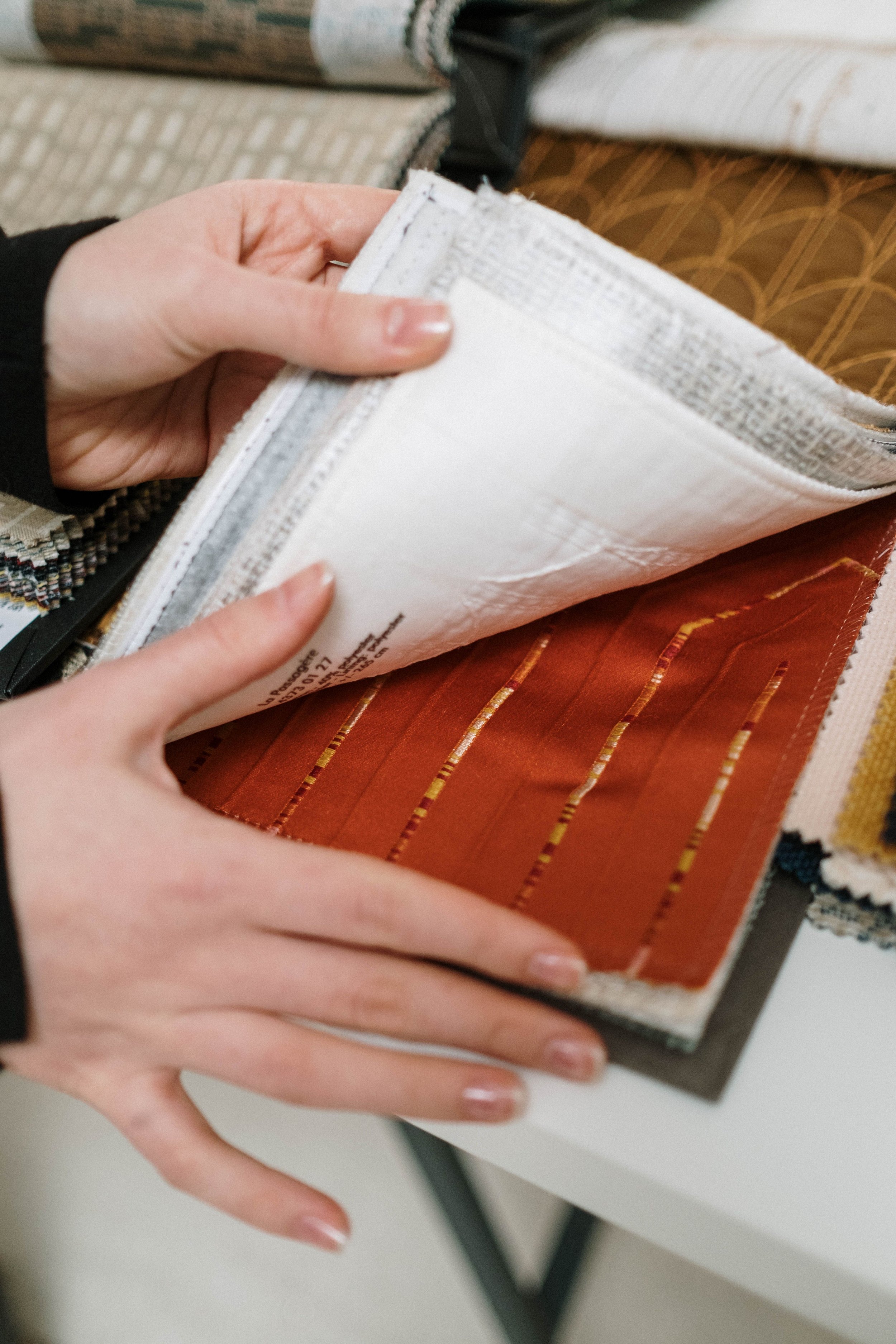Person holding an open fabric sample book showing various textiles and colors.