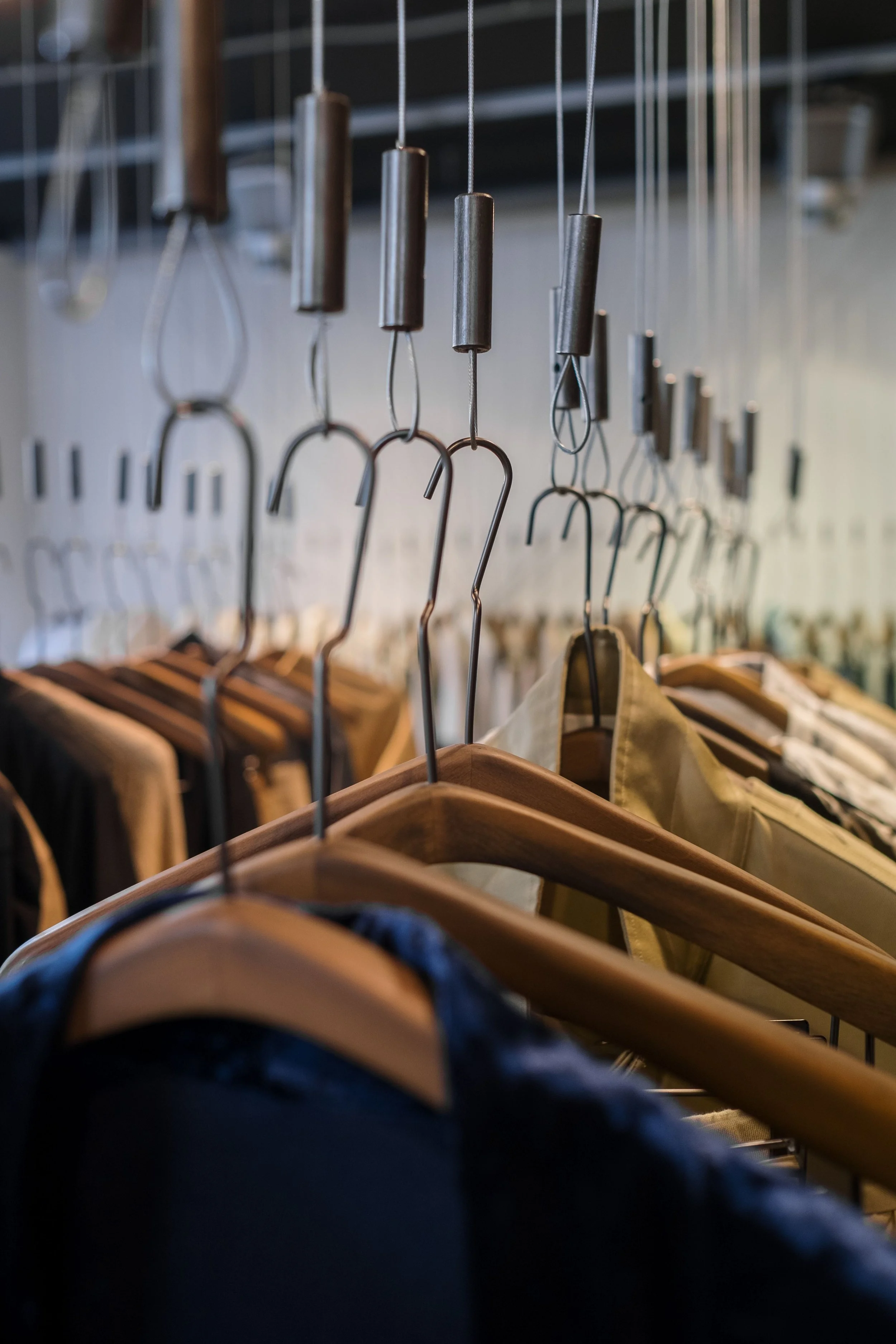 Hanging metal hooks and cylindrical weights above wooden hangers with clothing in a retail store.