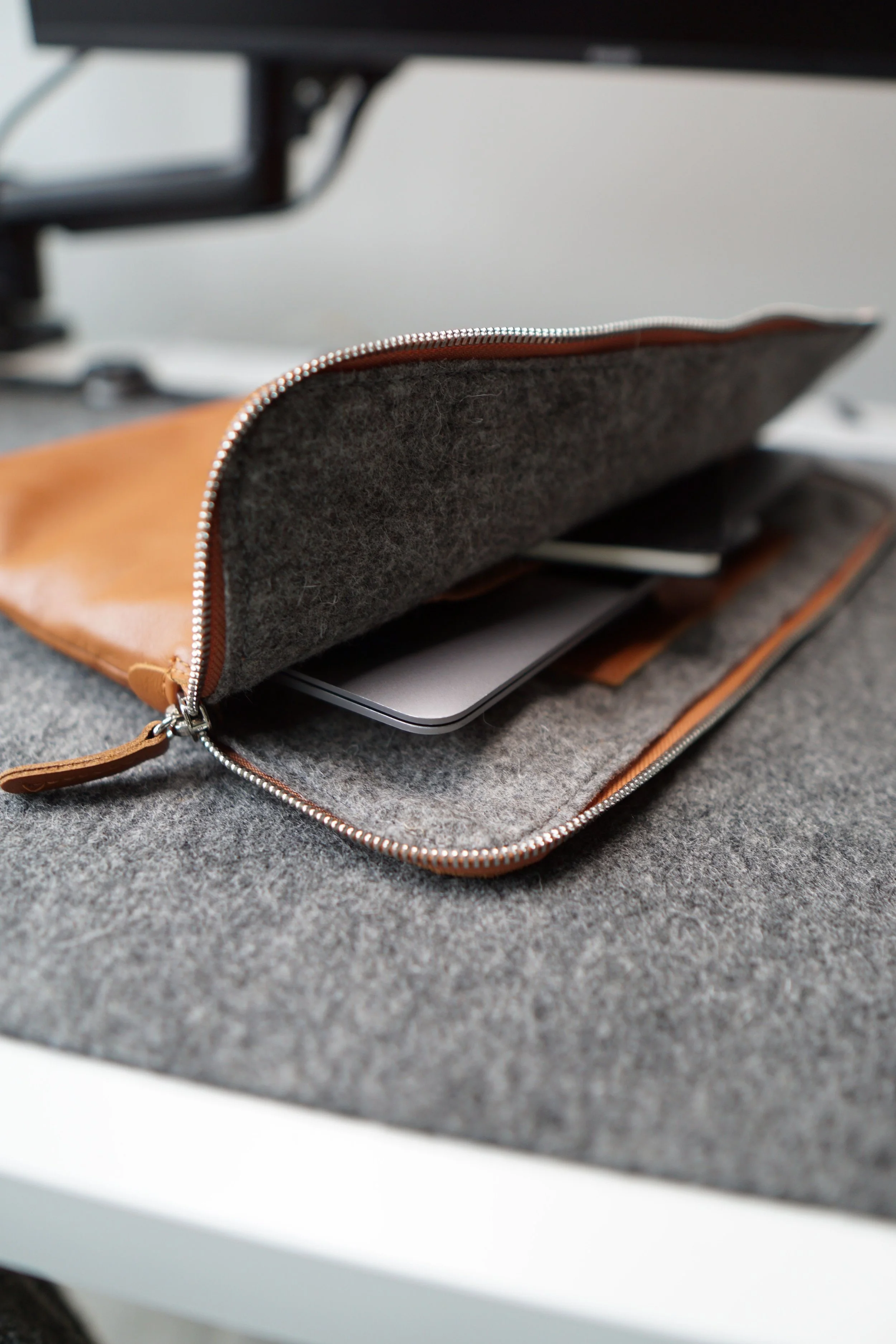 Close-up of an open wallet with a gray felt interior, placed on a dark gray surface, with a laptop partially visible underneath.