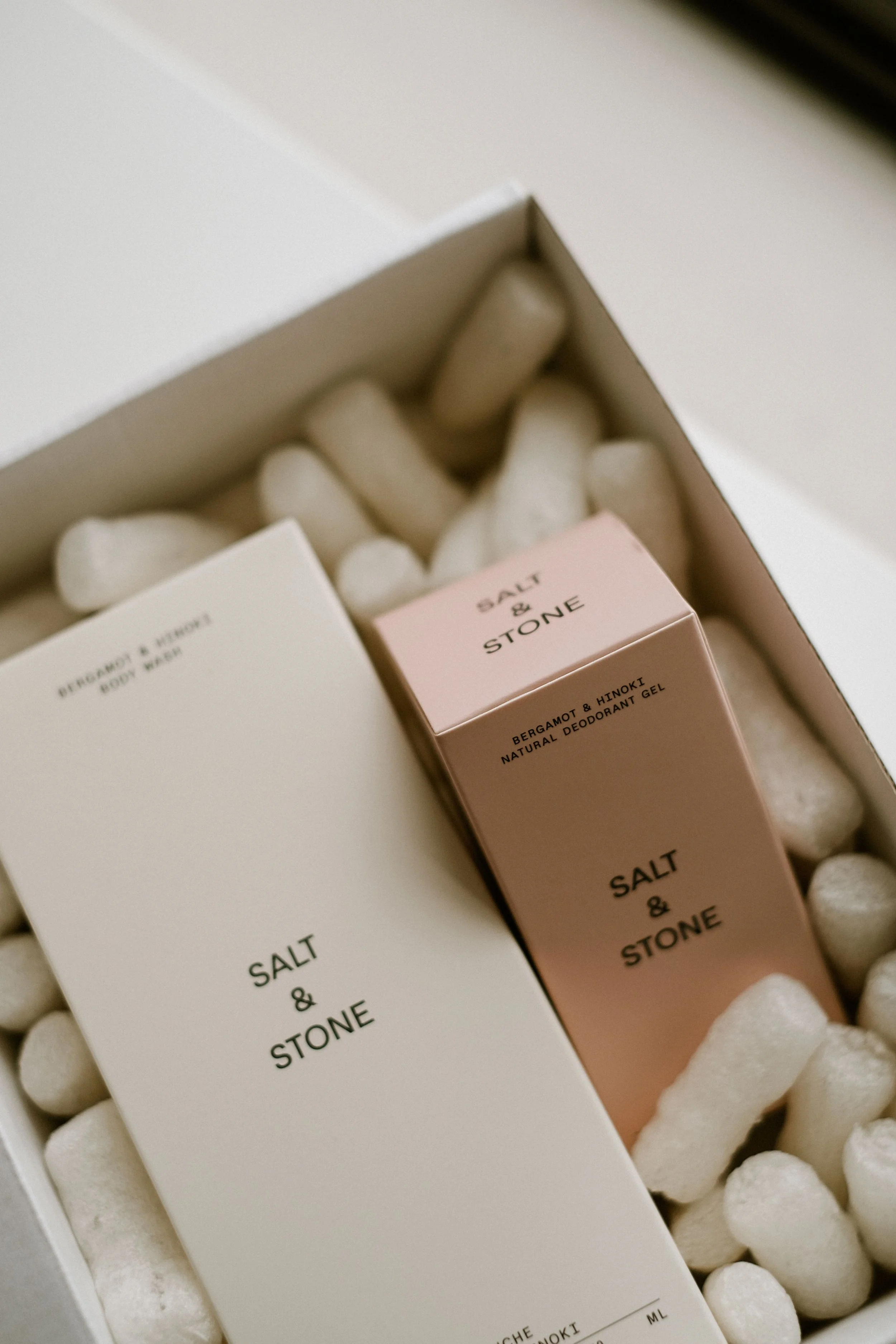 Close-up of a white box containing soap and deodorant products, with white packing peanuts filling the space around the items.