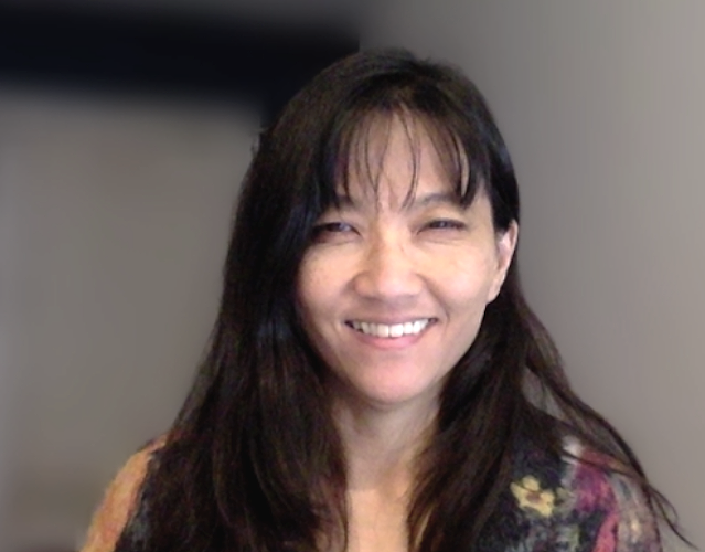 A woman with long dark hair smiling and looking at the camera.