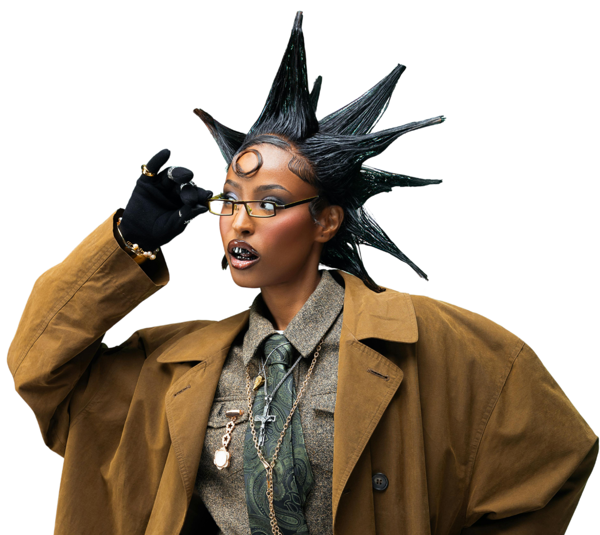 A woman with spiked black hair and glasses adjusting her glasses. She is wearing a tan coat, patterned shirt, tie, and several layered necklaces.