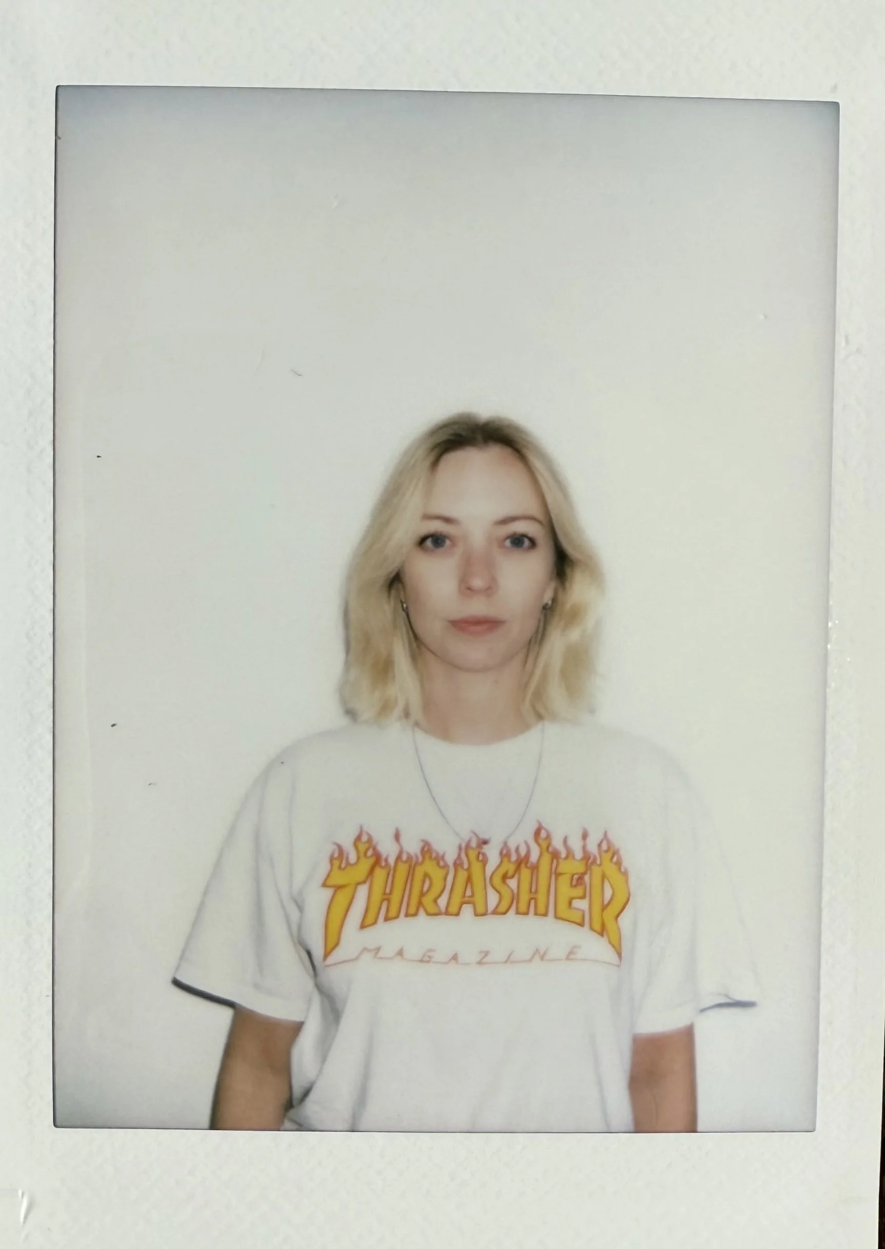 A woman with blonde hair wearing a white thrasher t-shirt.