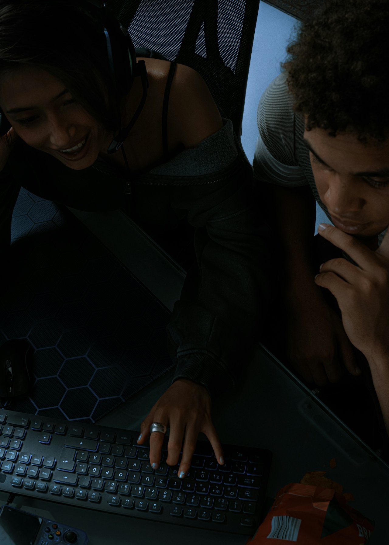 Deux jeunes personnes regardent un ordinateur portable, l'une d'elles pose la main sur le clavier, dans un environnement intérieur sombre.