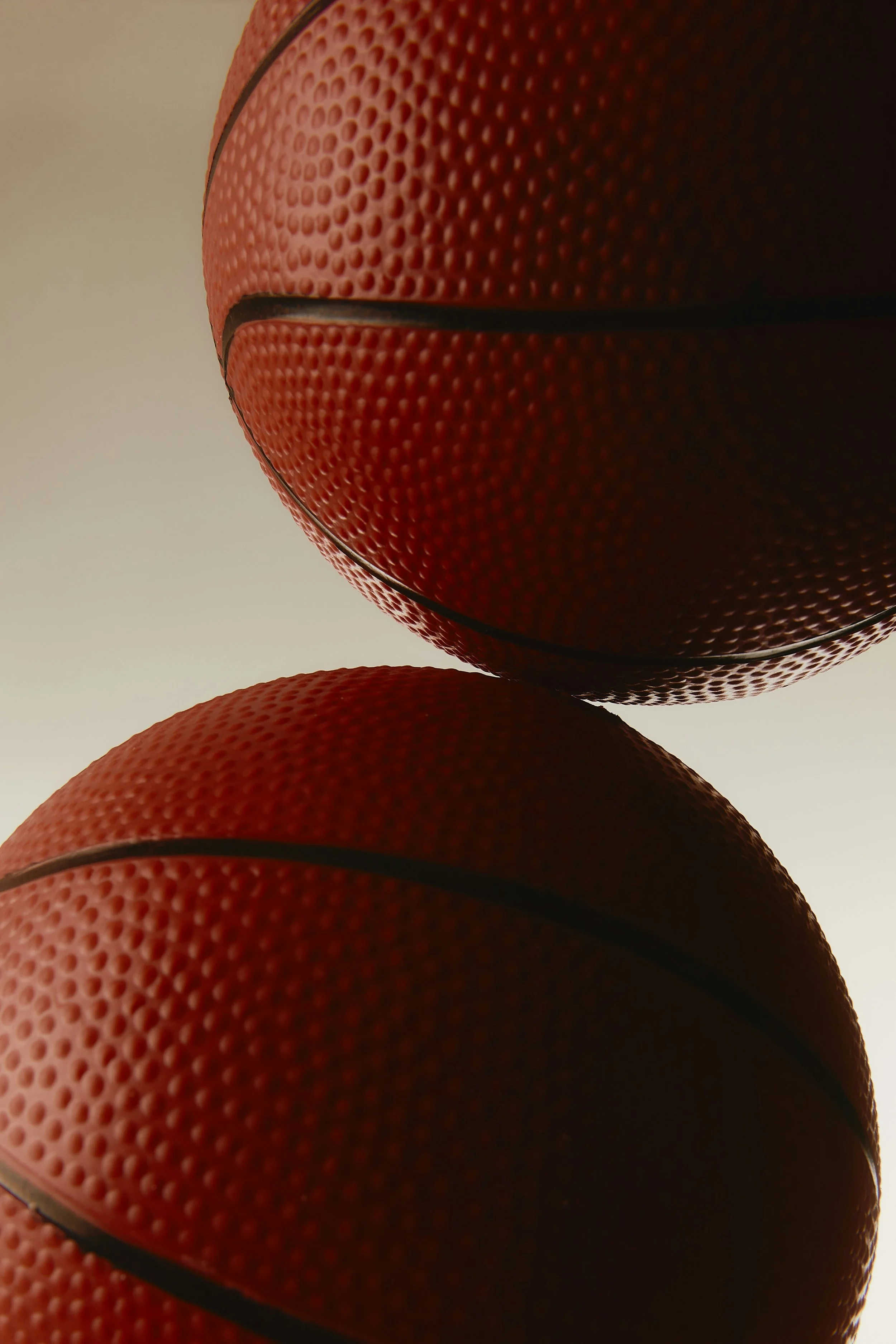 Une balle de basket-ball rougevue de côté et légèrement de dessus, avec une surface textured et des lignes noires, sur un fond blanc clair.