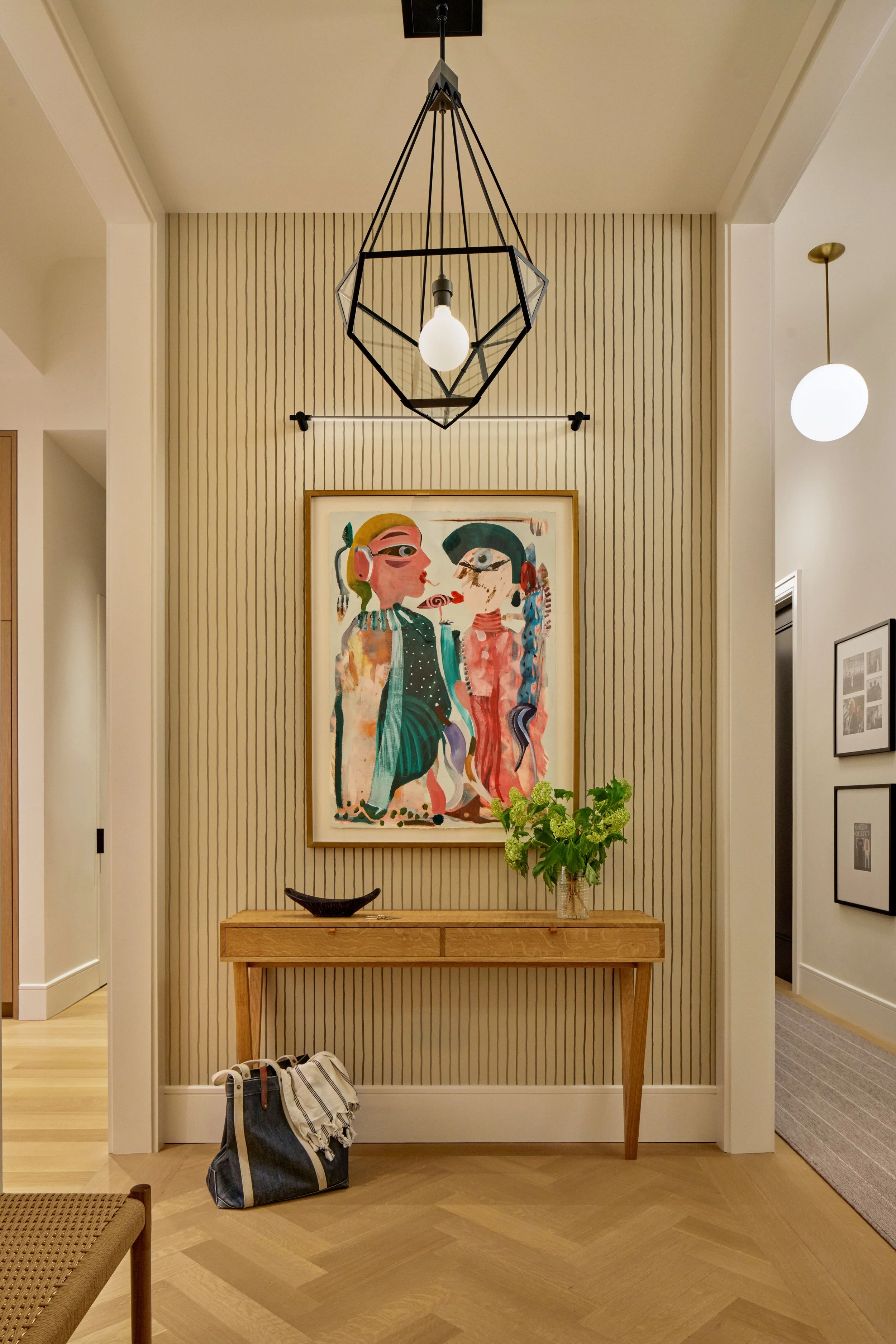 Interior entrance hallway with a wooden console table, a framed colorful abstract artwork on the wall with an art light above it, and Urban Electric Pendants.