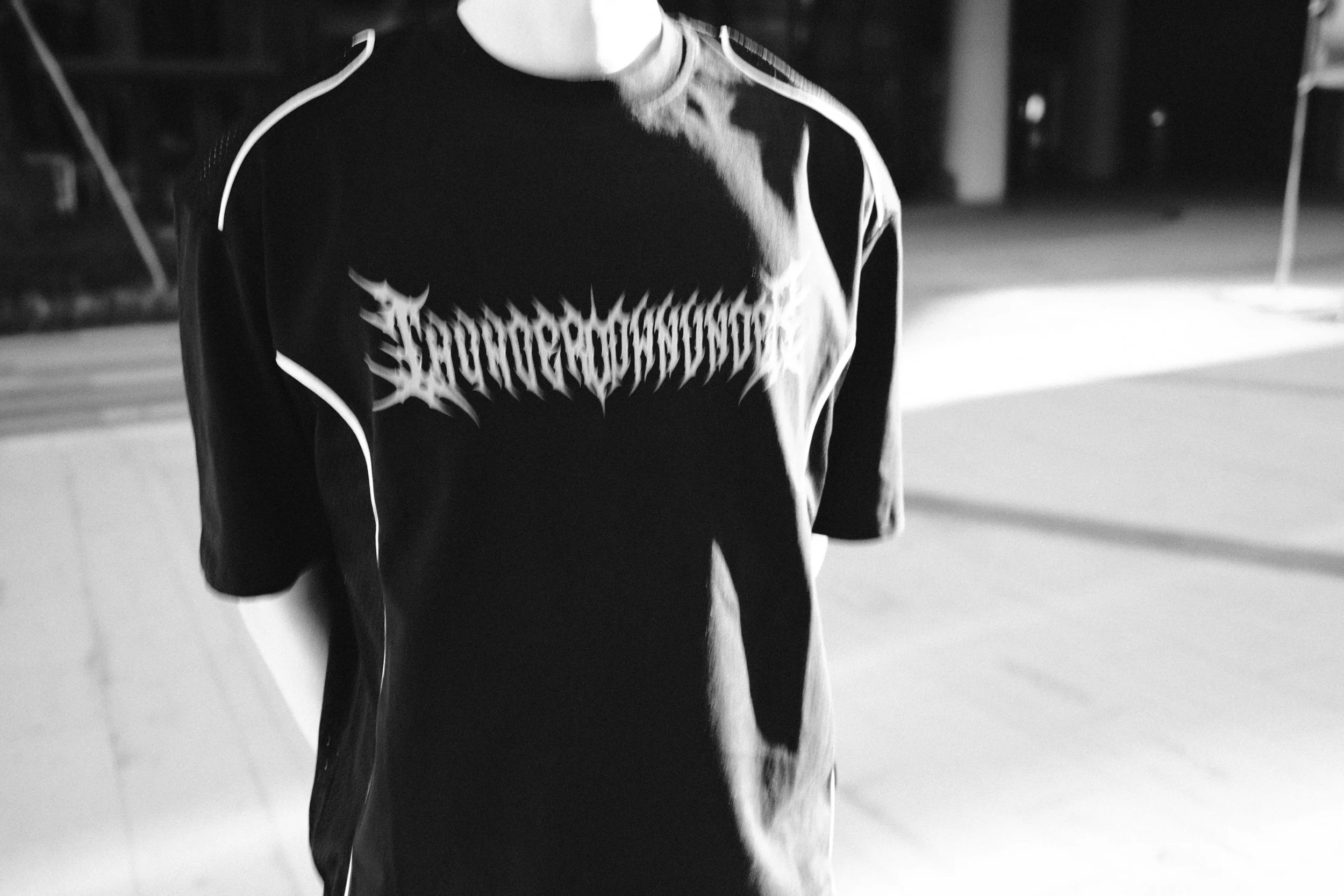 A person wearing a black shirt with a graphic design, walking outdoors on a sidewalk at night.