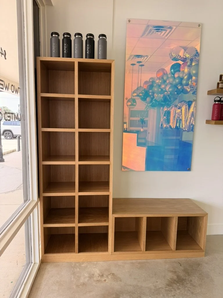 Wooden storage unit with closed cubbies, topped with gray water bottles, beside a bench with open cubbies, in a room with a colorful balloon decoration reflected in the mirror.