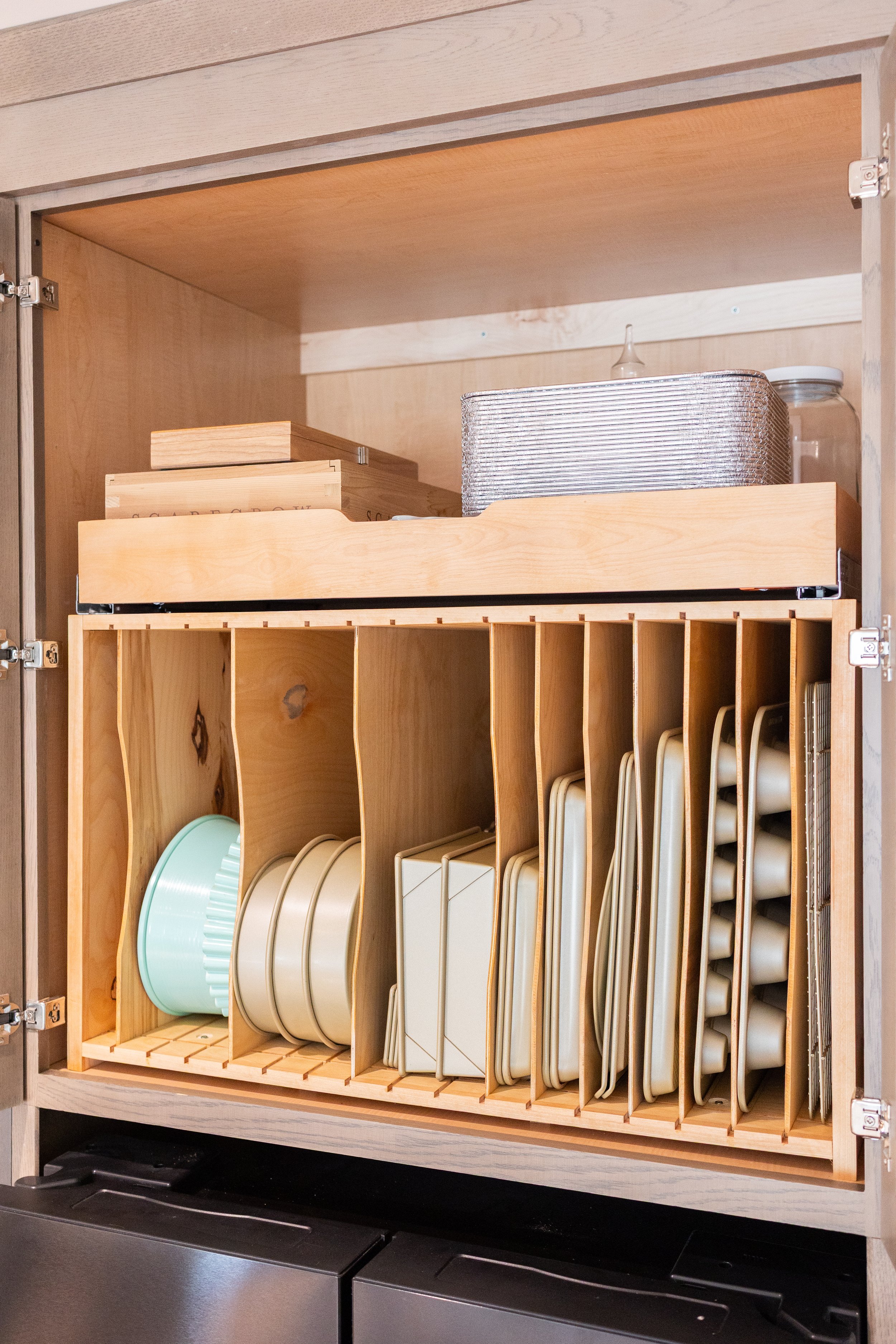 A wooden kitchen cabinet with sliding doors open, showing dishes, plates, bowls, and kitchenware organized in cubbies.