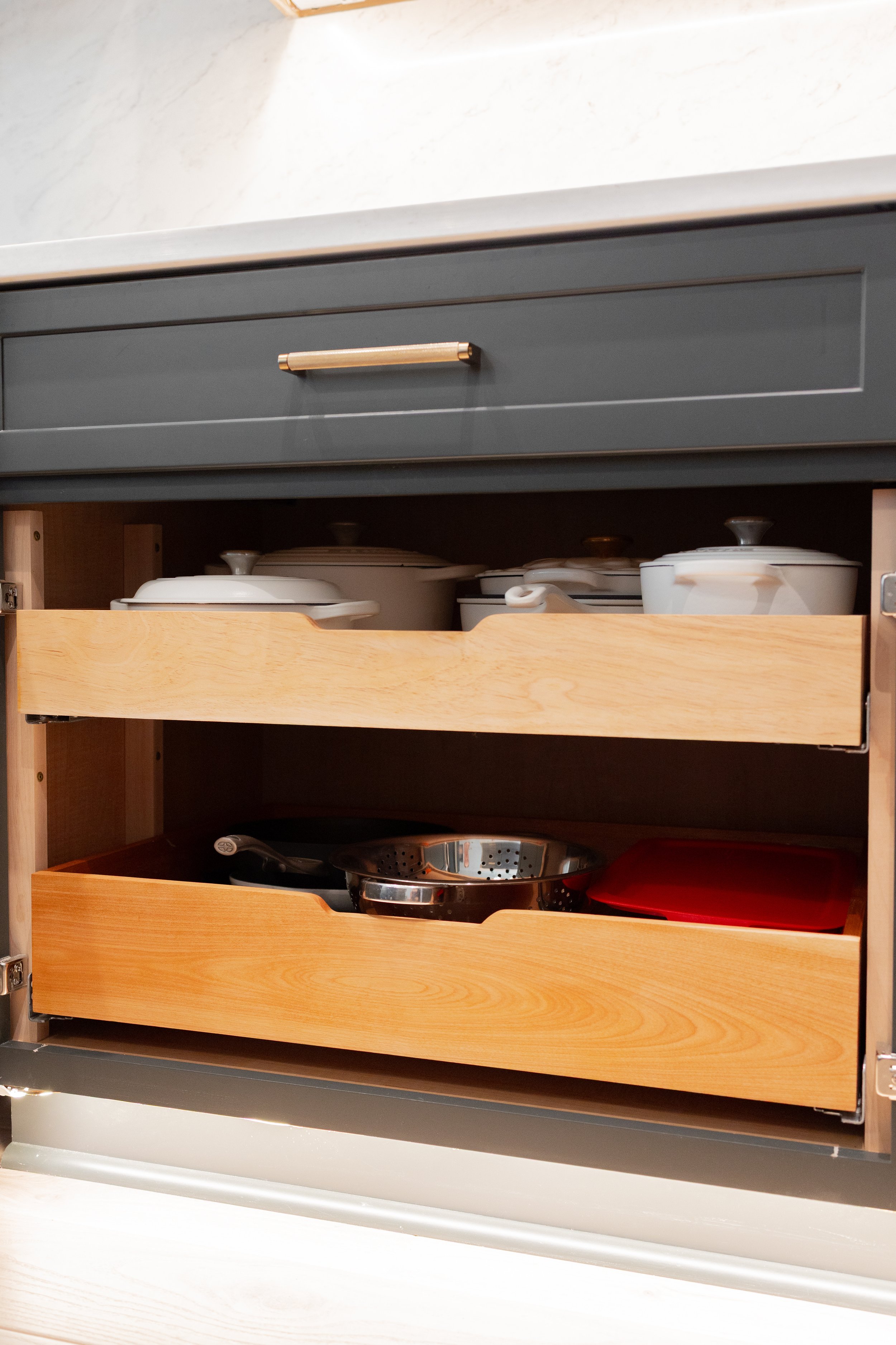 Kitchen cabinet with two drawers. The upper drawer is closed, and the lower drawer is partly open, revealing various kitchenware such as pots, pans, and a red cutting board inside.