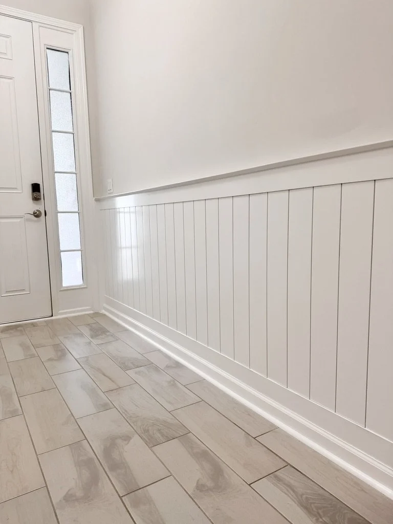 Entryway of a house with a white front door, sidelights, and wood-look tile flooring in a neutral color.