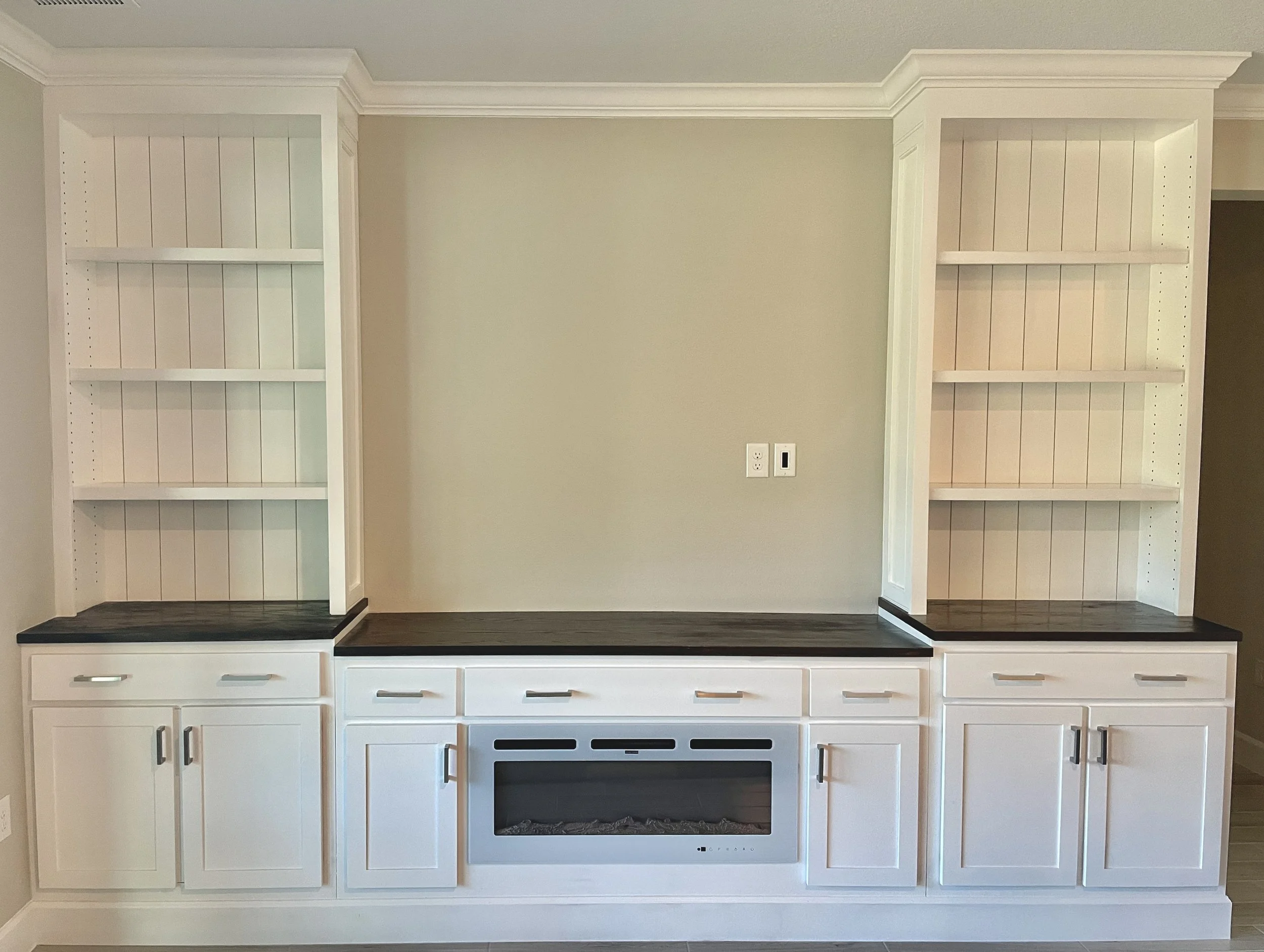 Empty white built-in kitchen cabinets with drawers and shelves, a black countertop, and a white stove with a black oven.