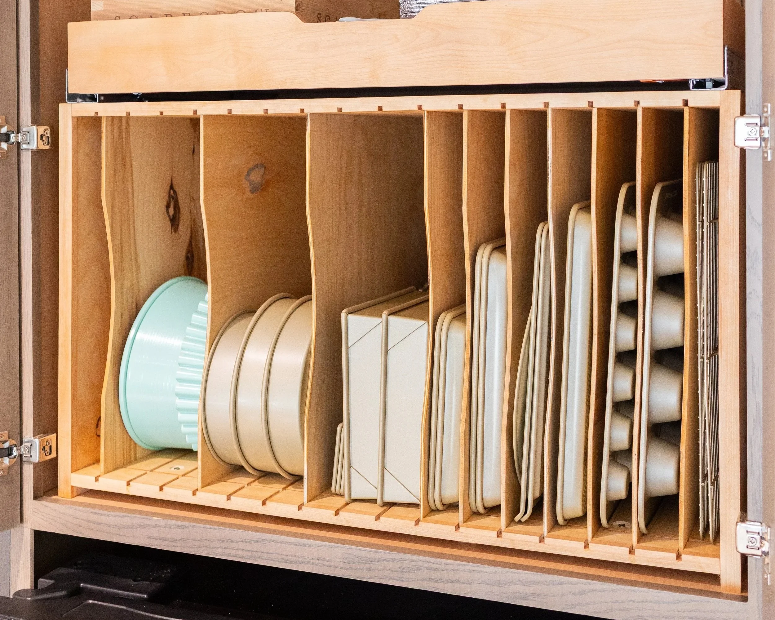 Wooden kitchen cabinet with divided slots containing various plates, bowls, and ceramic dishes.
