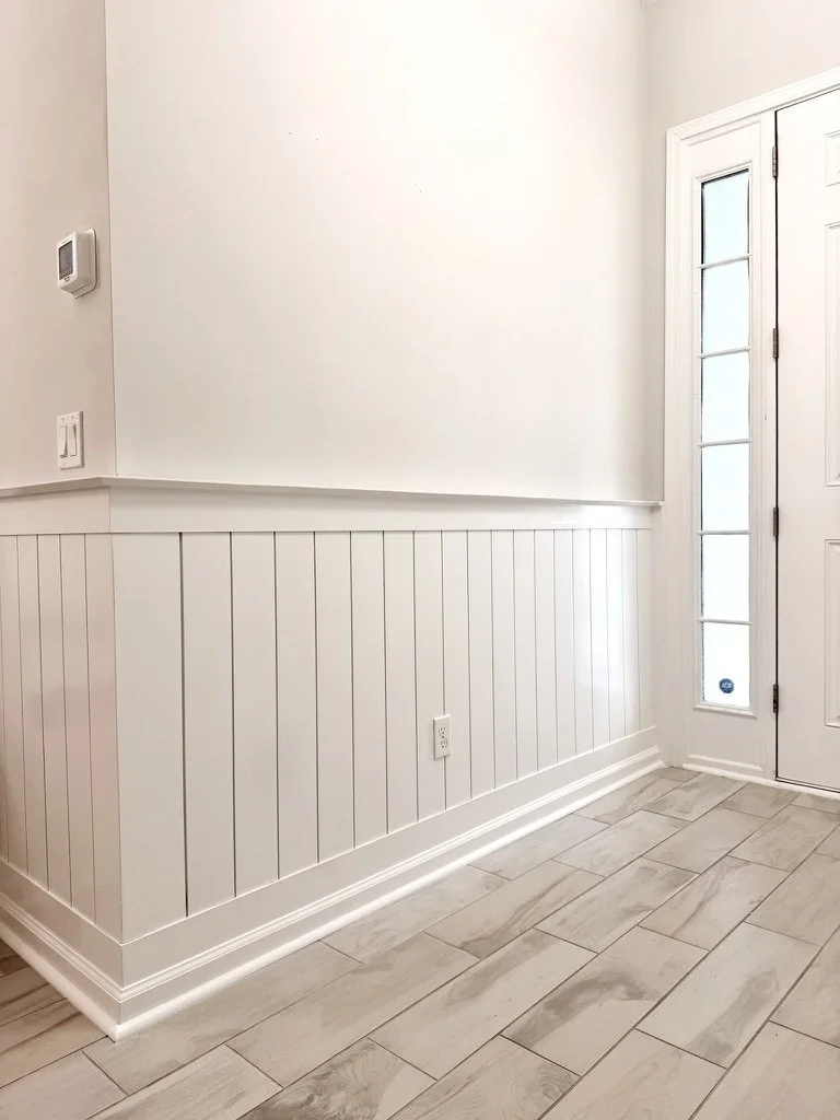 Entryway with white wainscoting on the lower half of the wall, a white door with a glass panel, tile flooring, and a thermostat on the wall.