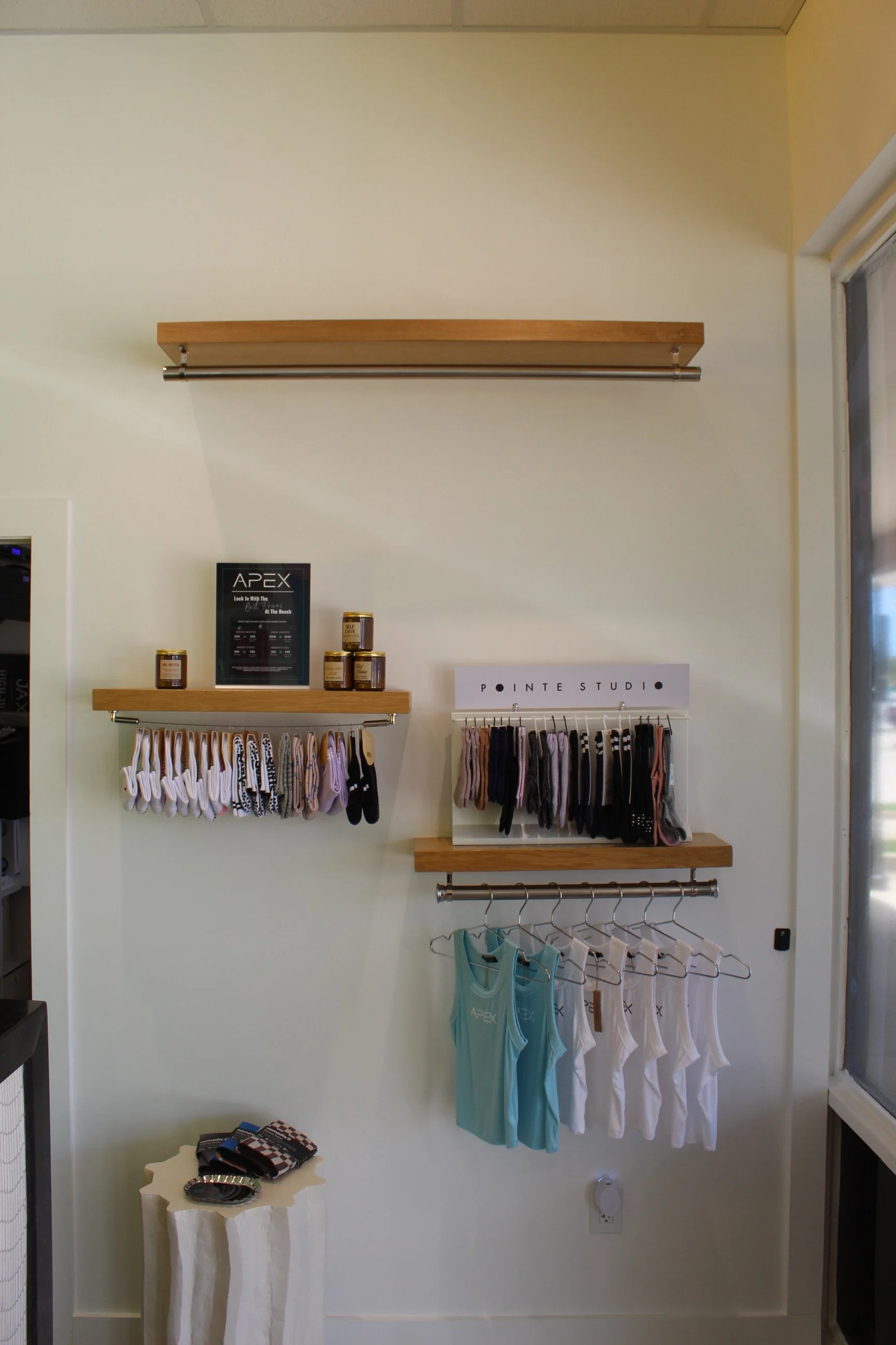 Clothing store display with socks on two shelves, tank tops on hangers, and a wall sign that reads 'Pointe Studio'.