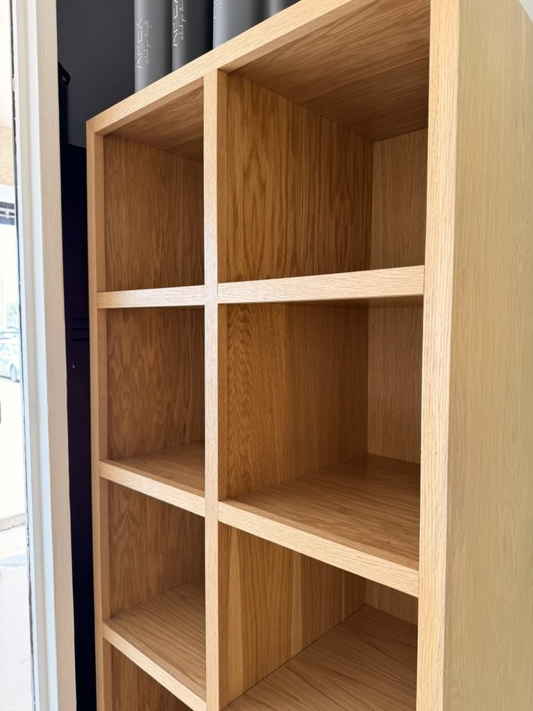 Empty wooden shelf unit with six compartments near a window.