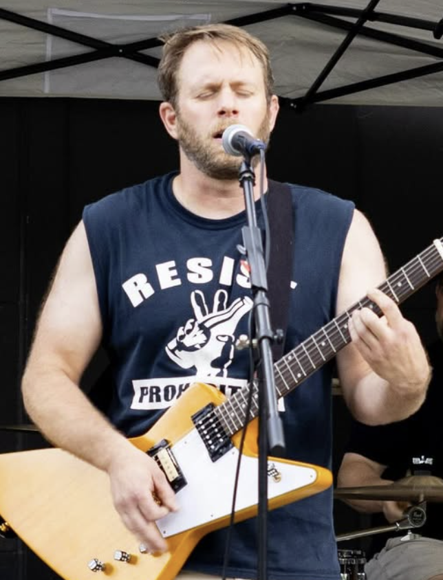 A man with closed eyes singing into a microphone while playing a yellow electric guitar during a performance.