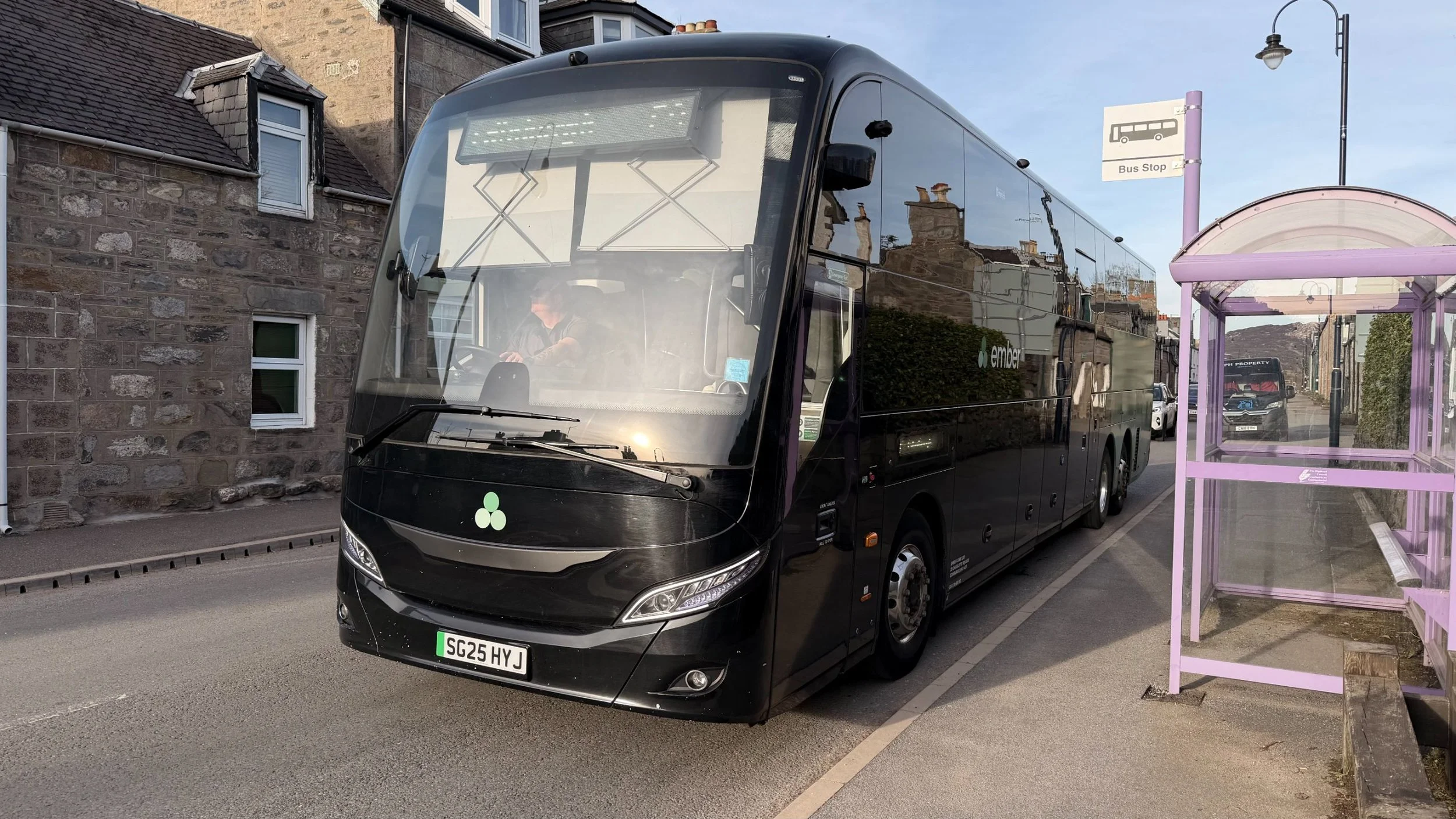 Ember electric coach SG25 HYJ stopped on Main Street, Newtonmore — direct service from Edinburgh Airport and Inverness, zero-emission travel into the Cairngorms