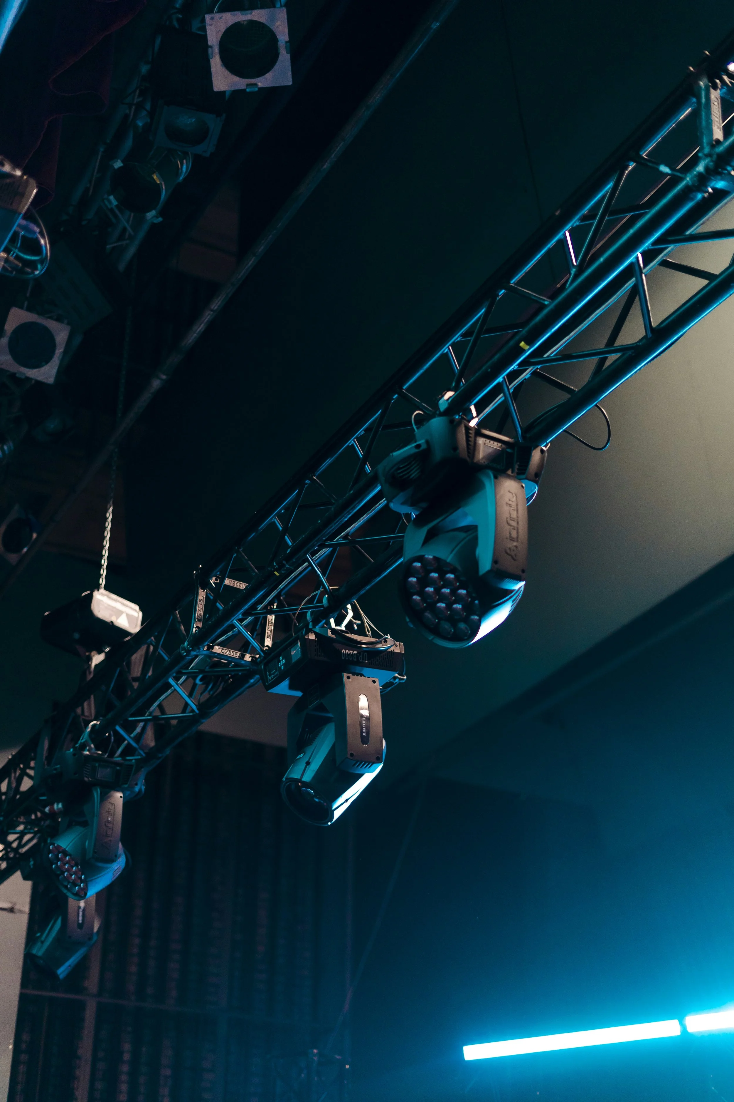 Stage lighting equipment including multiple LED stage lights mounted on a metal truss, with a dark background and some illuminated areas.