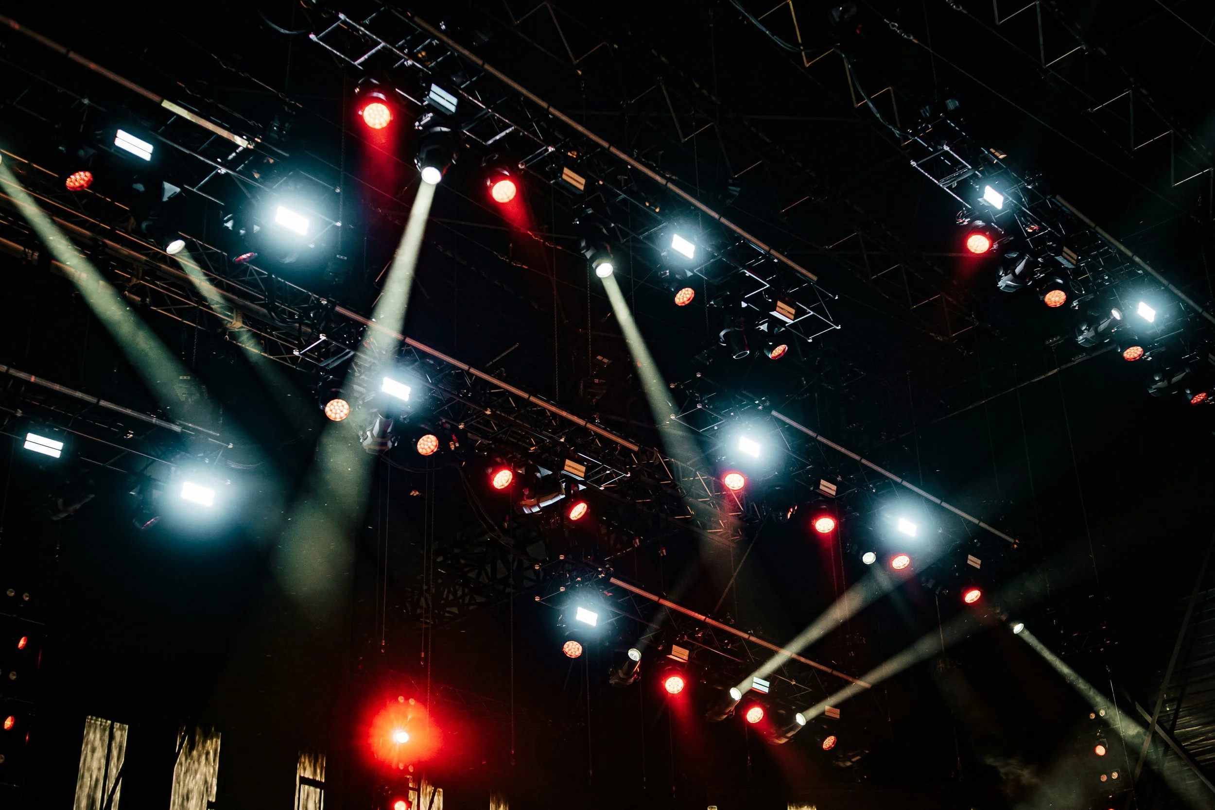 Stage lighting with multiple spotlights, red and white lights, and a black ceiling grid.