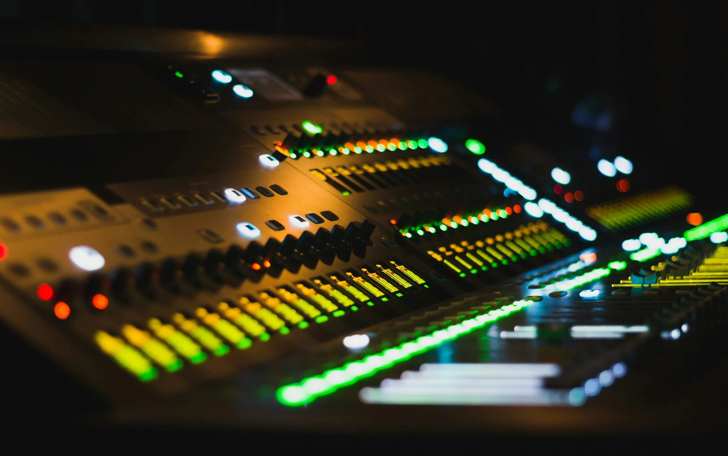 Inside view of a digital audio mixing console with colorful illuminated controls at night.