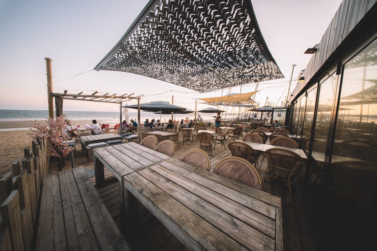 Terrasse de café plage avec des chaises en rotin, parasols, et vue sur la mer, en soirée