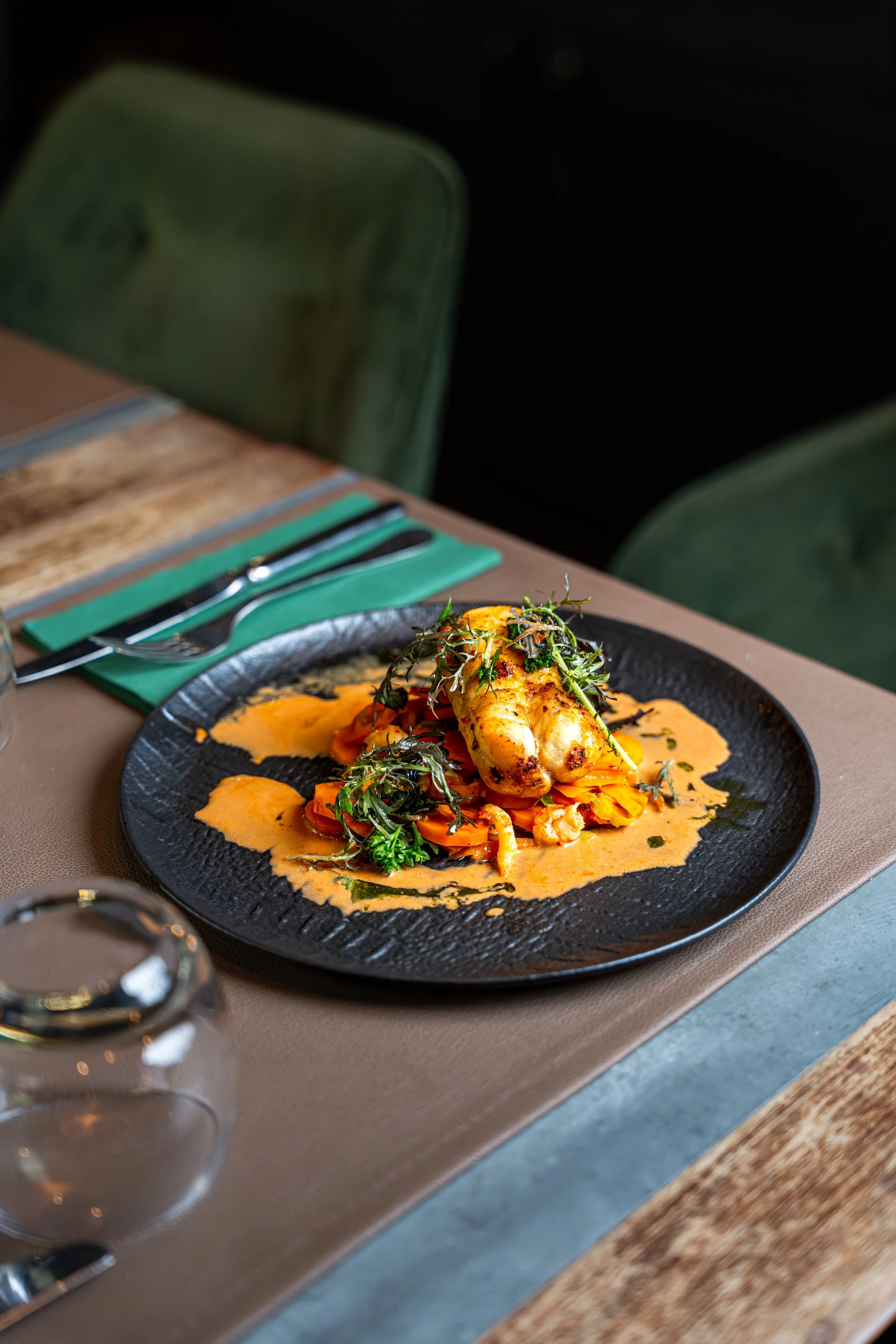 Assiette de poulet rôti avec sauce, légumes et garniture verte, sur une table dans un restaurant.