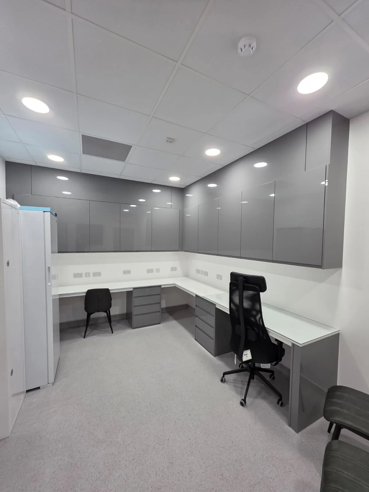 Empty office cubicle with gray cabinets, white desk, and black office chairs in a modern office space.