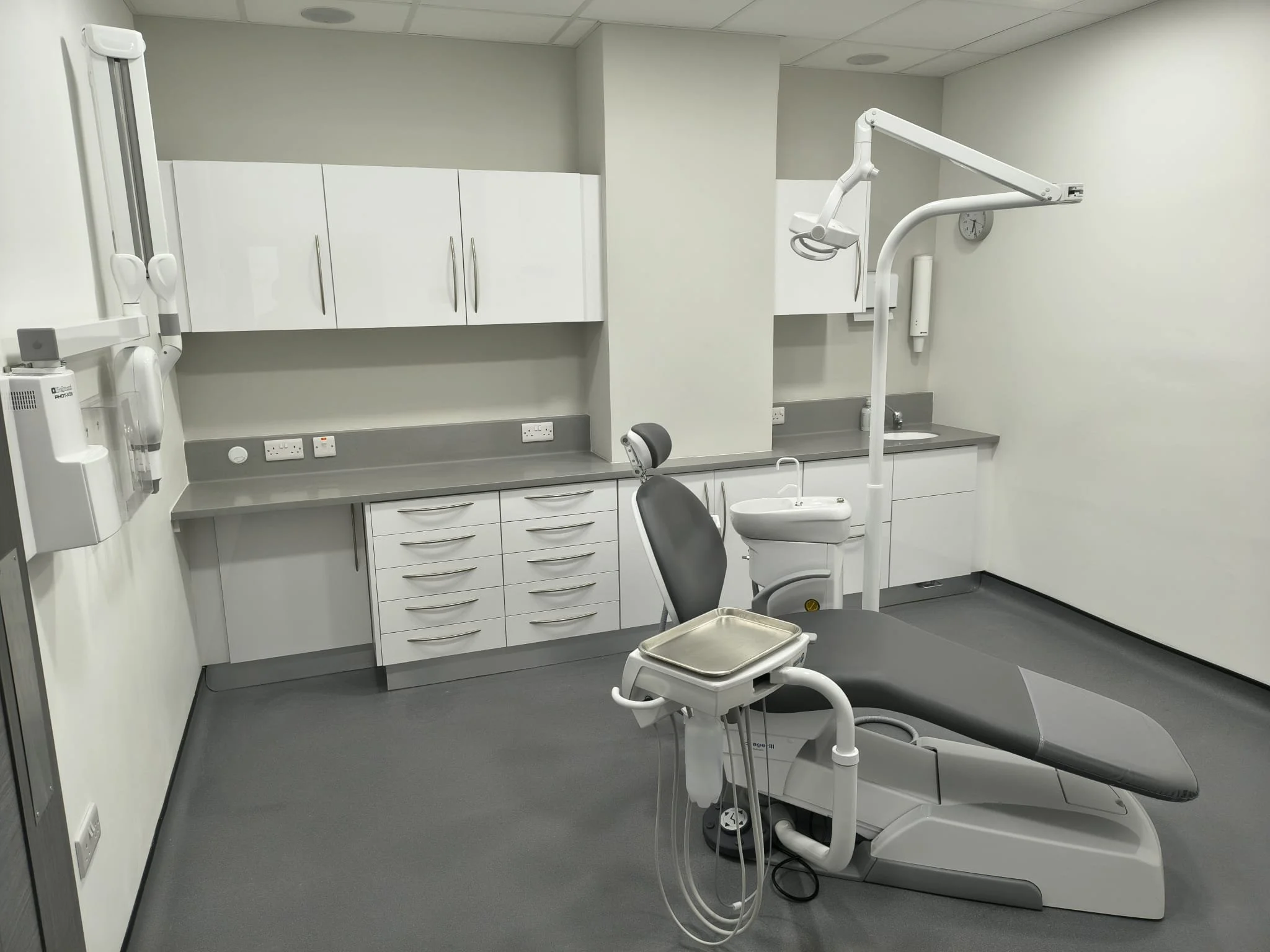 A dentist's office with a dental chair, overhead light, cabinets, and dental equipment.
