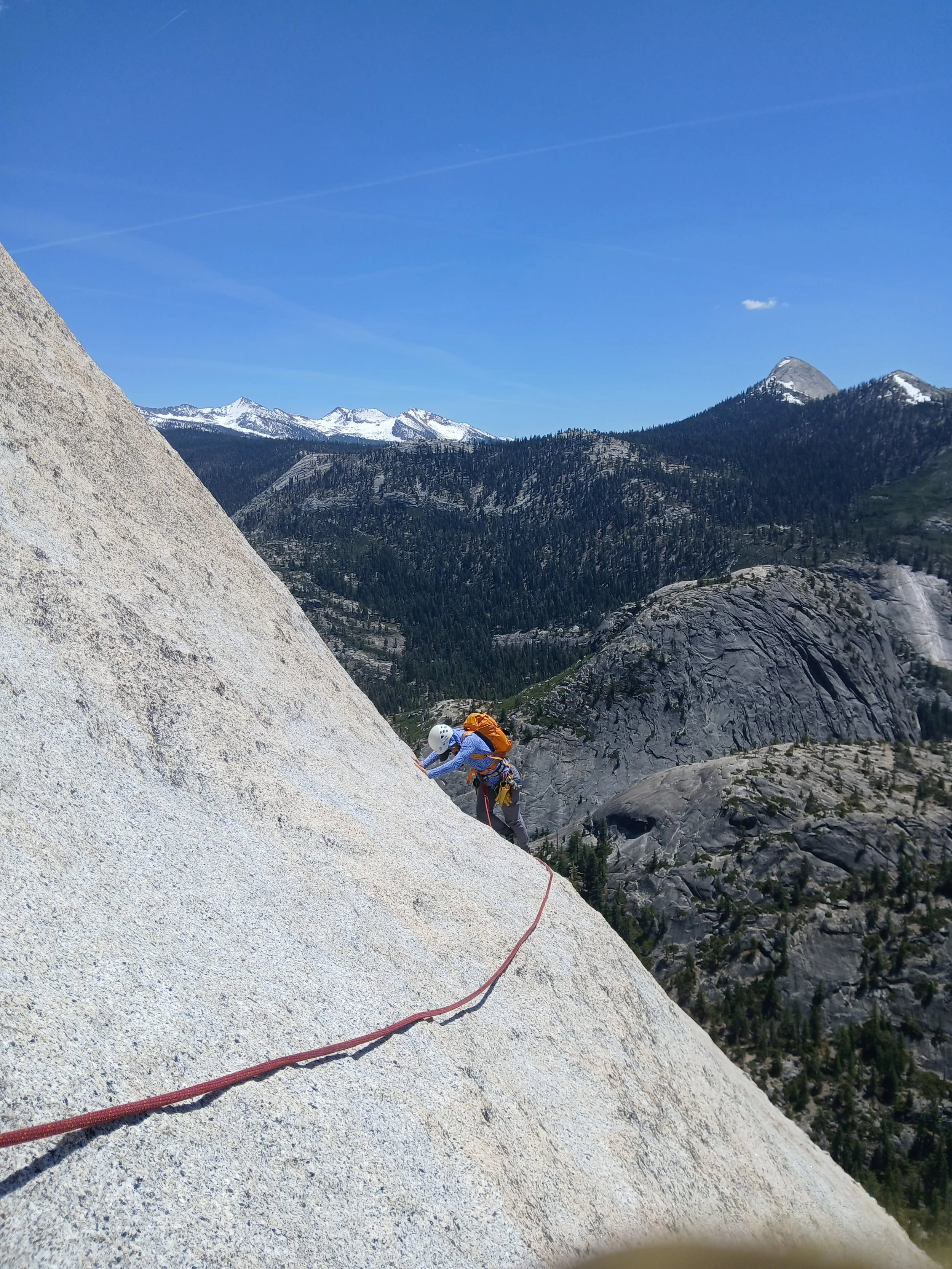 Lori is rock climbing with snow-capped mountains in the background of the photo