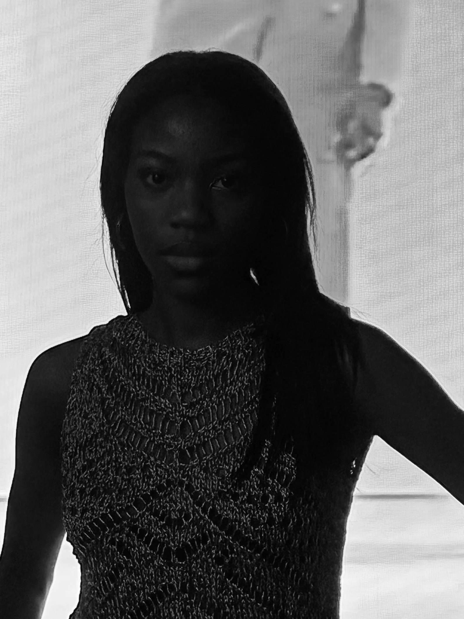 A grayscale photo of a woman with long hair, wearing a textured top, standing against a plain background.