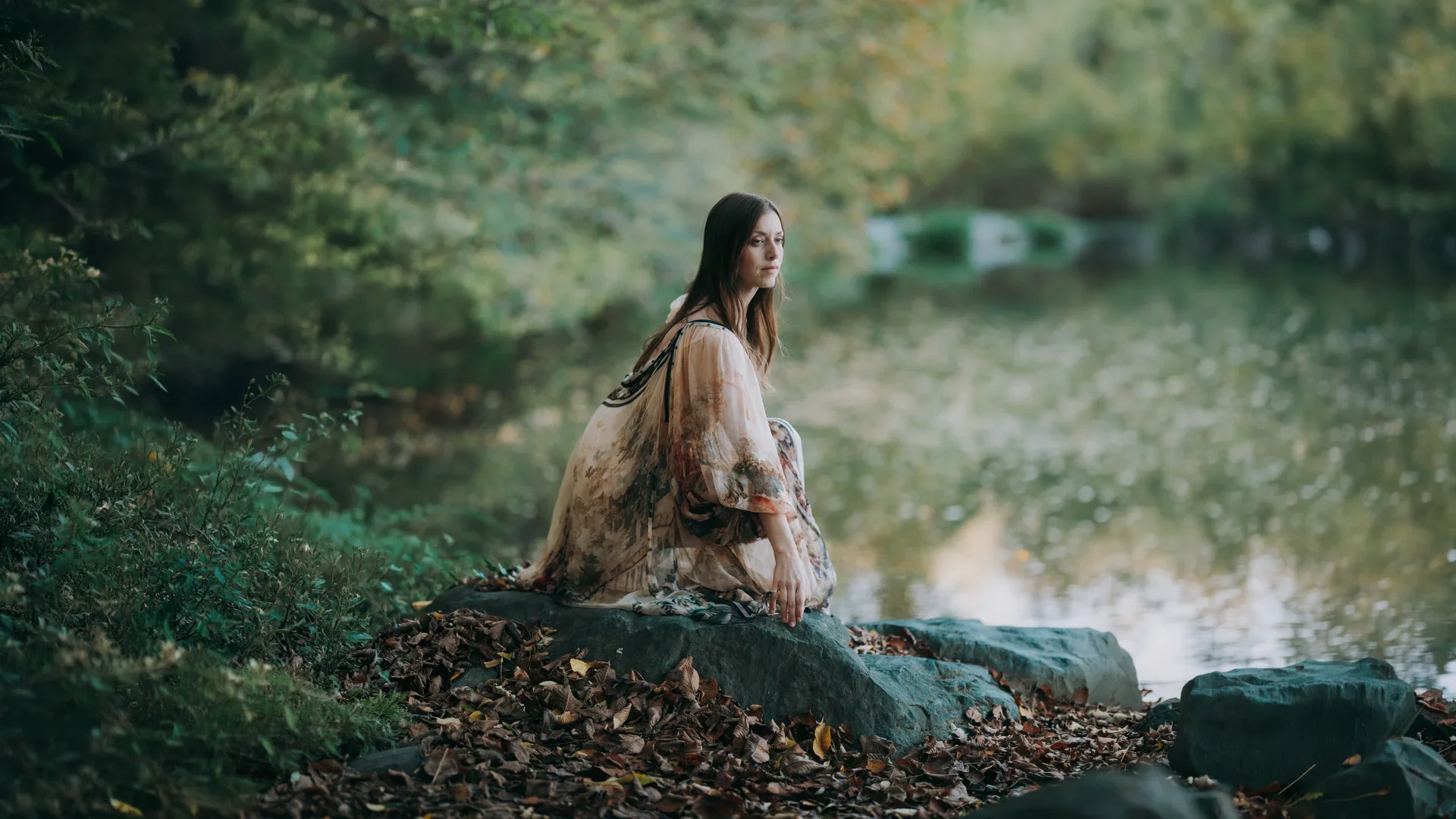 woman-boho-painted-dress-rocks-serene-lake-forest-landscape-1920w.webp