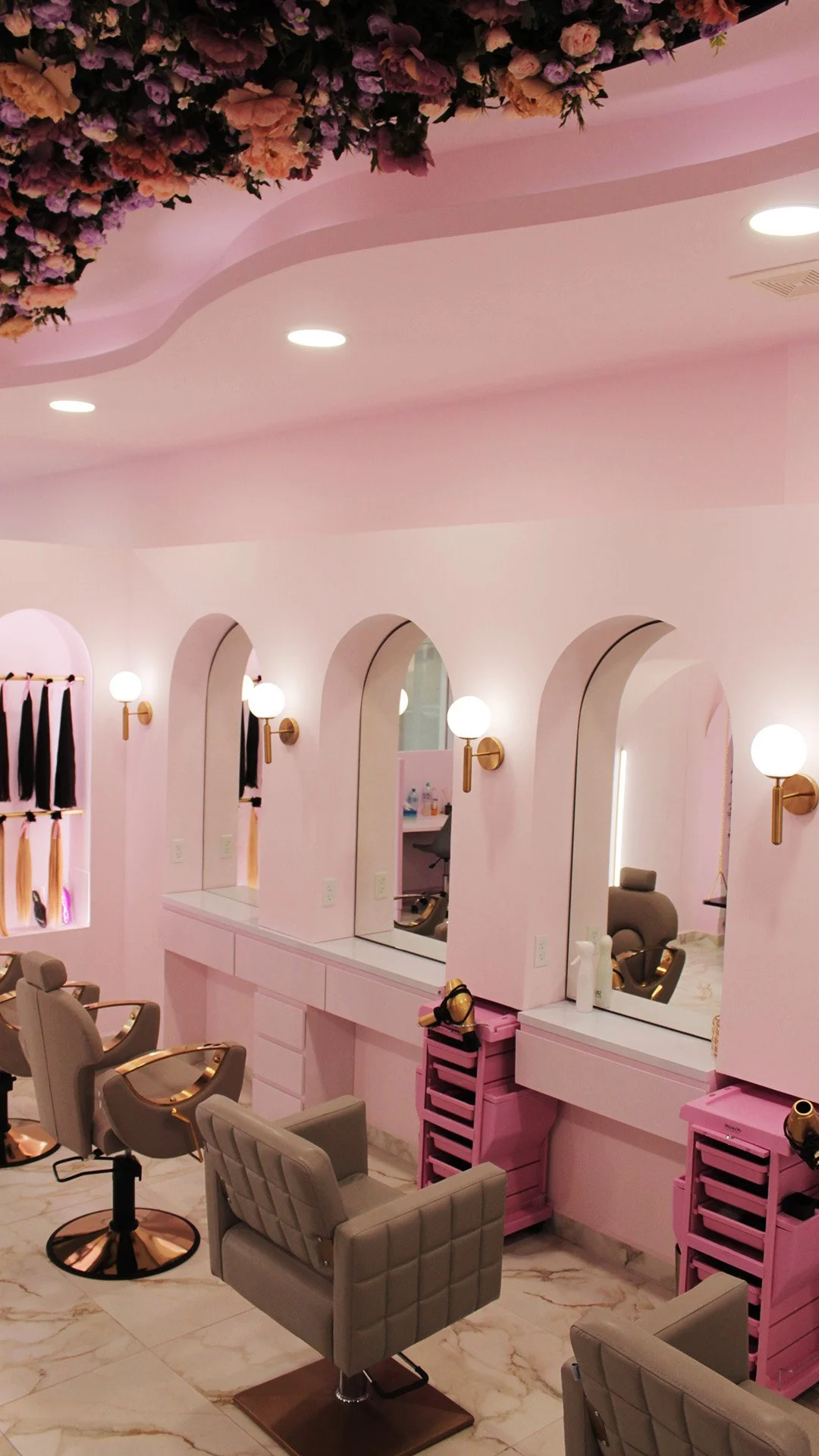 Interior de salón de uñas o belleza con paredes rosas, espejos, lámparas de pared, sillas de color gris y robots de manicura rosas.