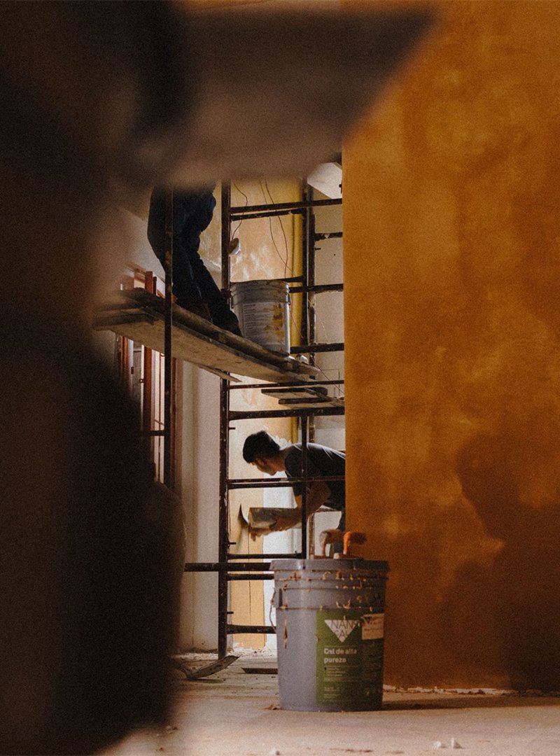 Dos personas trabajando en una construcción interior con andamios y pintura amarilla en las paredes.