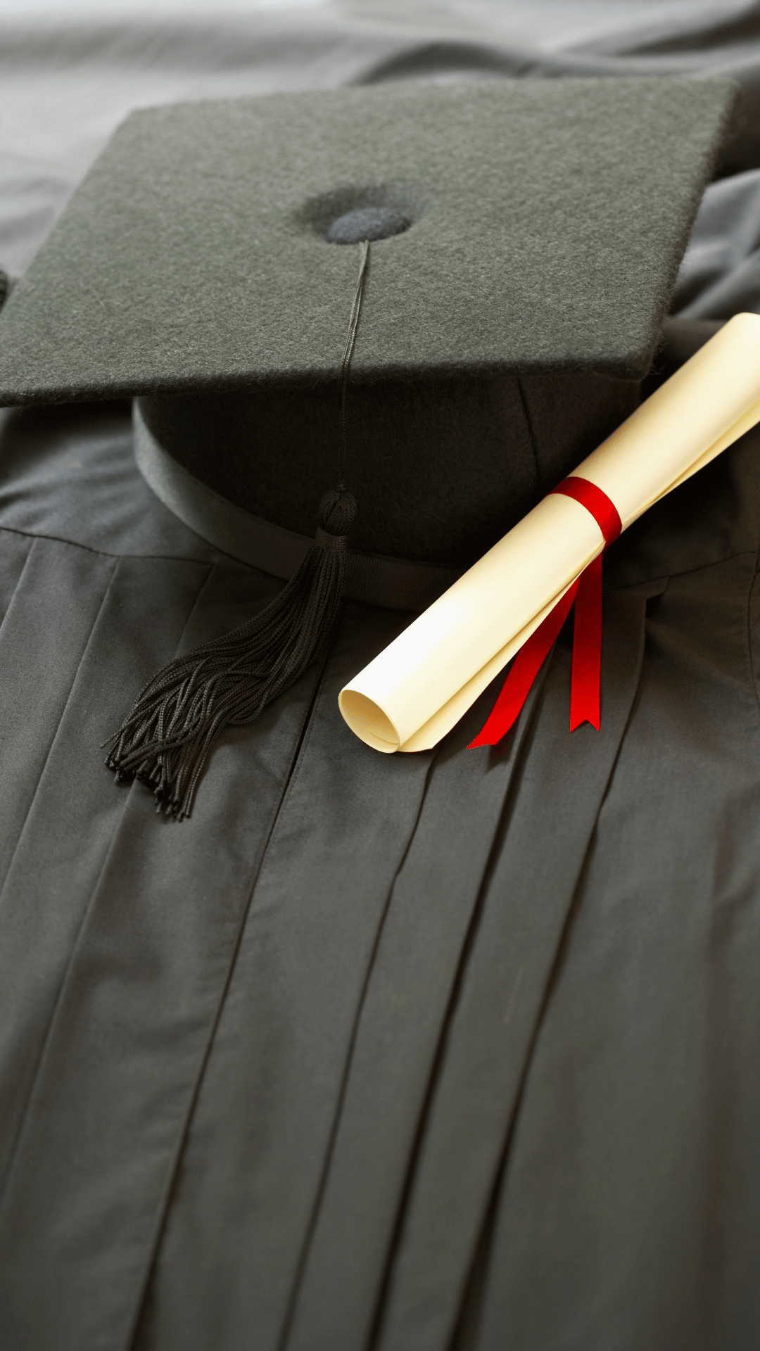 Graduation cap and diploma on a fabric surface.