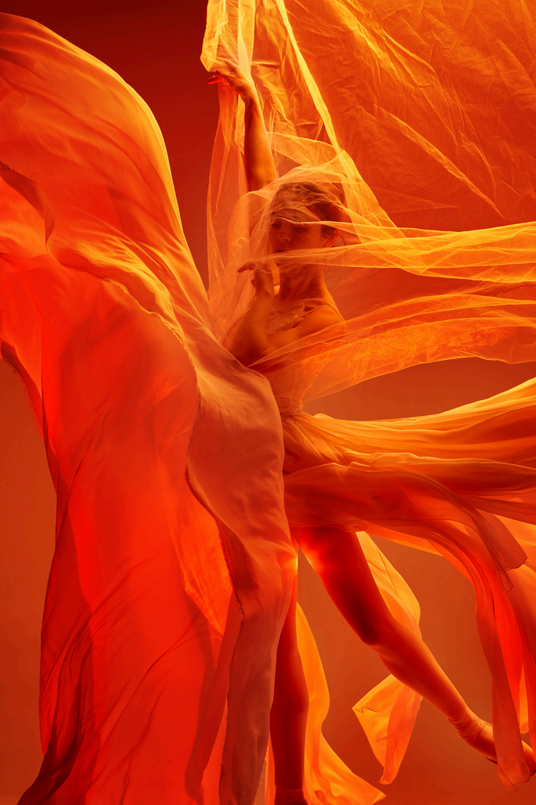 Une danseuse entourée de tissu orange fluide, créant un effet dynamique et artistique.