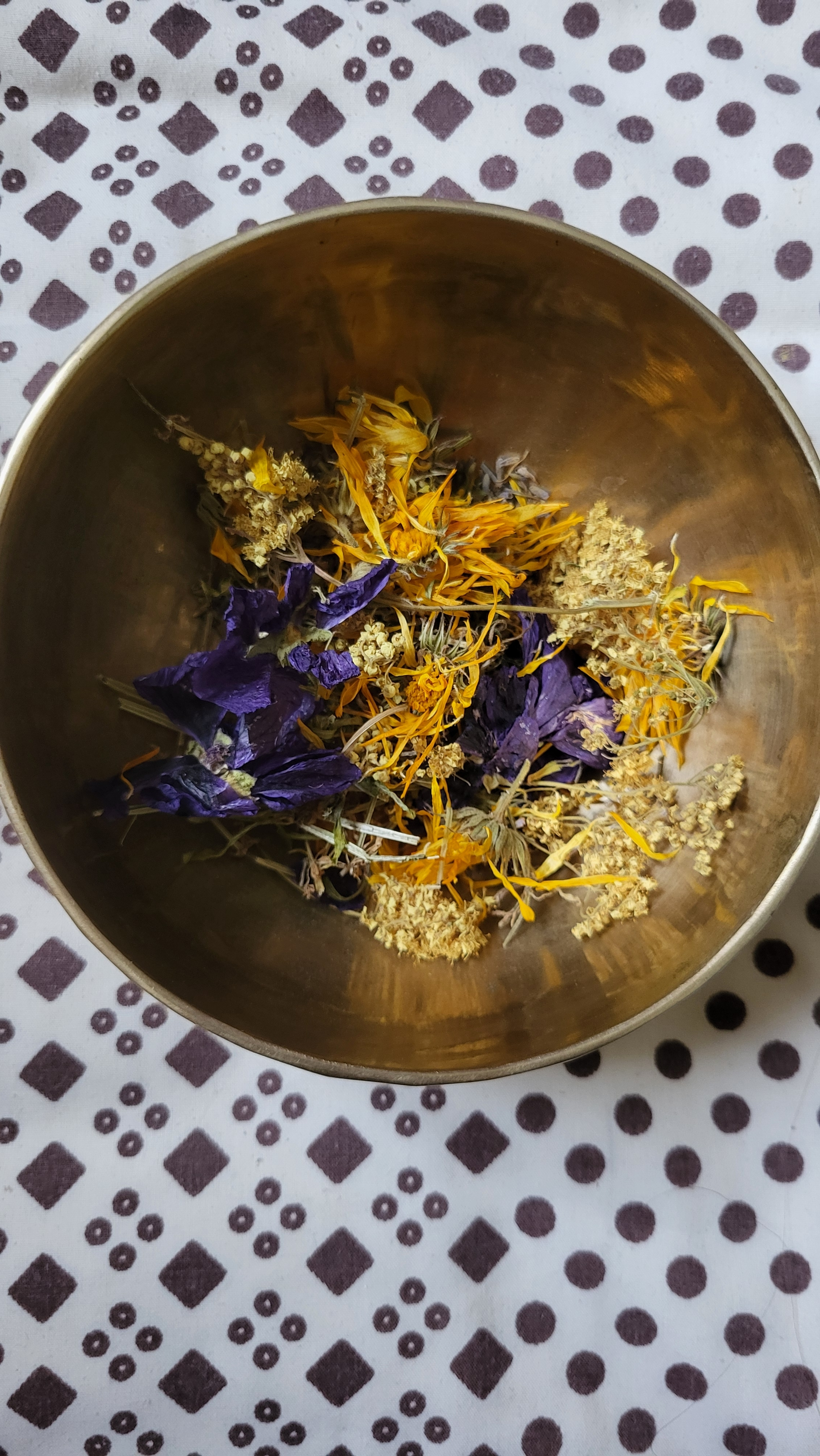 Bouquet de fleurs séchées dans un bol en métal, posé sur une table à motif géométrique en violet et blanc.