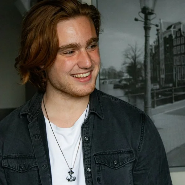 Portret van Matthijs, oprichter van Schaken Met Matthijs en het YouTube kanaal Matthijs Chess, glimlachend in een donkere spijkerblouse en wit T-shirt.
