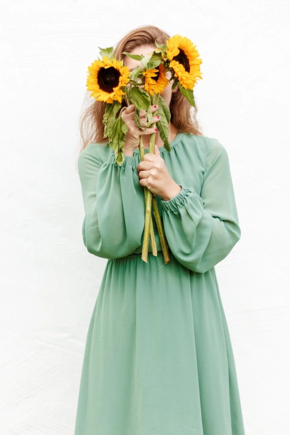 A woman in a light green dress holding a bouquet of sunflowers in front of her face.