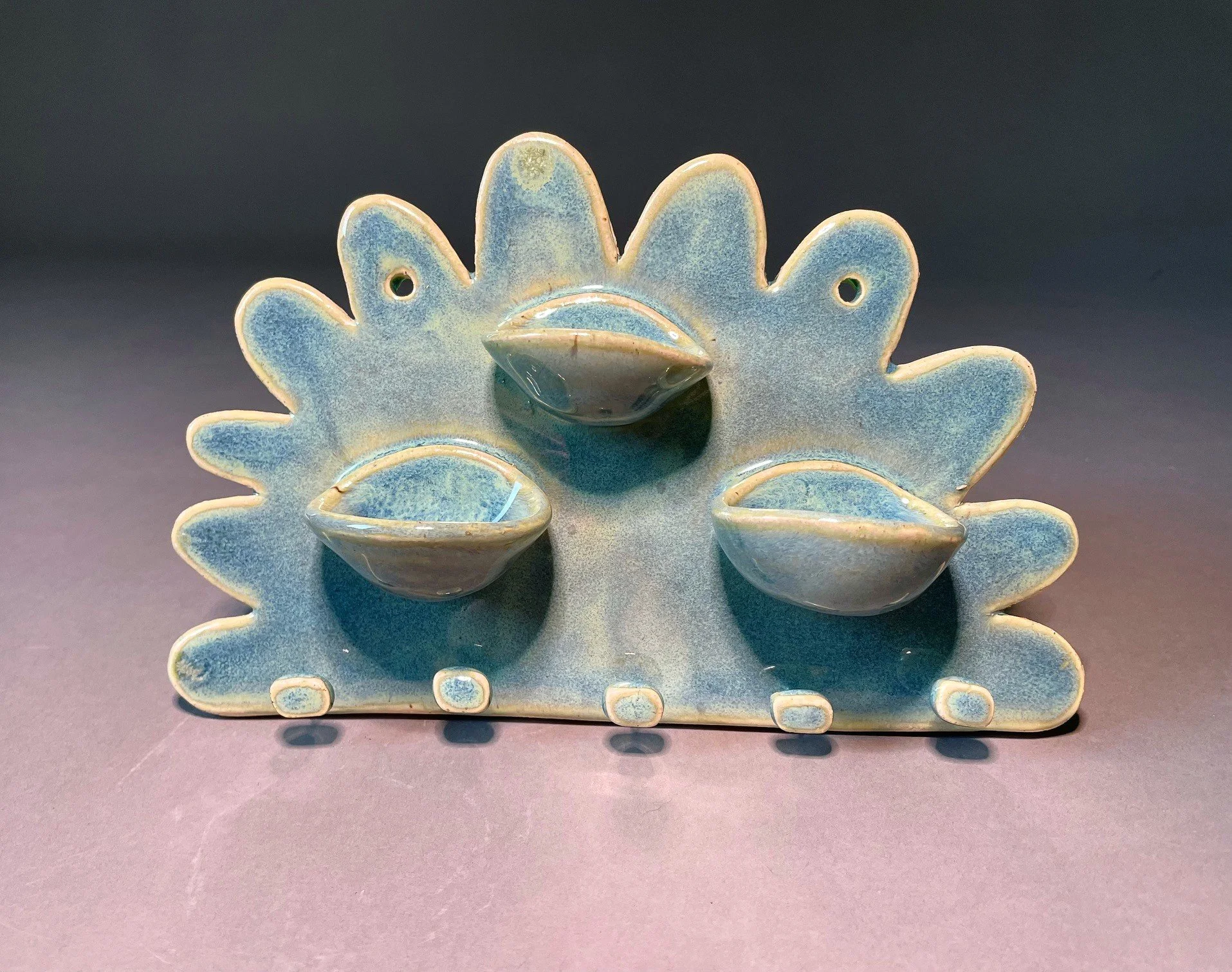 A ceramic jewelry holder shaped like a half flower (organic shape) with three small bowls in the center and 5 knobs for hanging necklaces. 