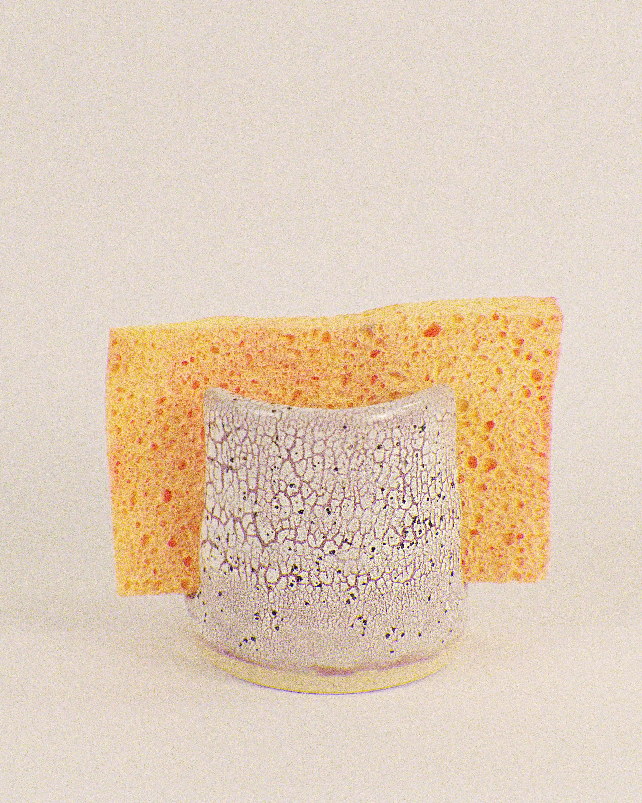 purple and white pottery sponge holder against a plain background.