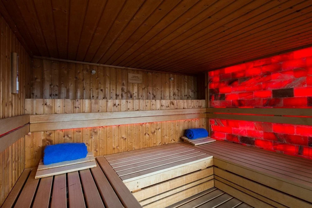 Interior of a wooden sauna with red salt bricks on one wall, blue towels on wooden benches.
