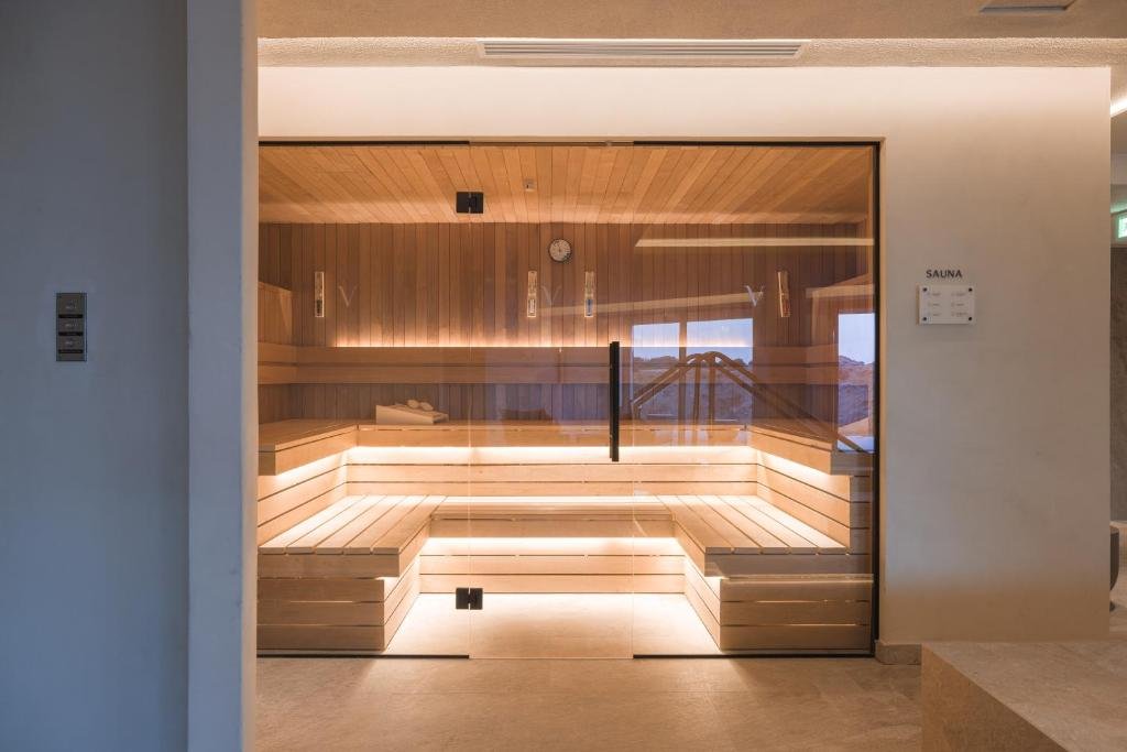 A modern indoor sauna with wooden benches and glass walls, illuminated with soft lighting.