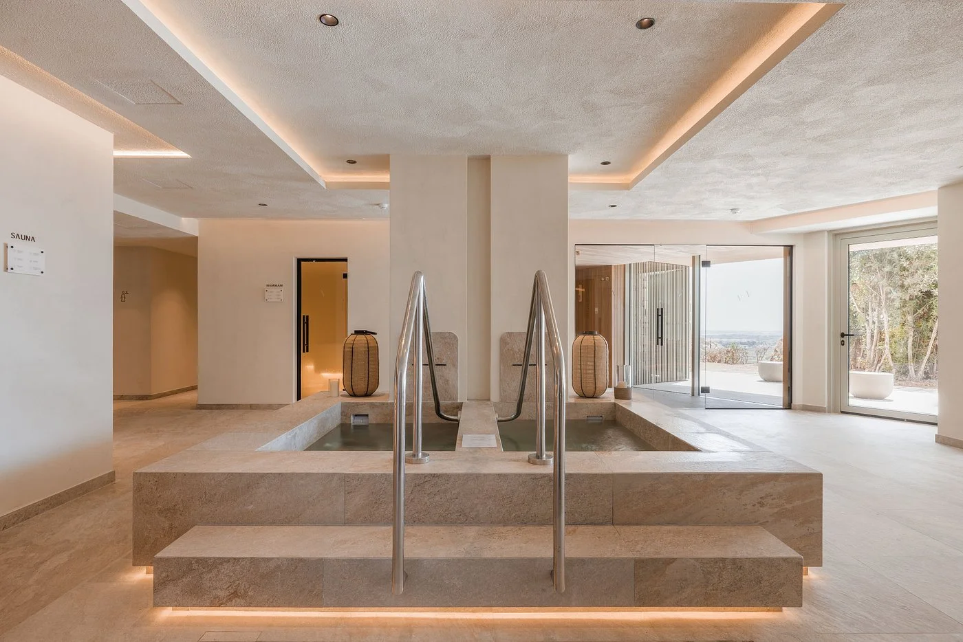 Modern indoor spa with a small indoor pool, wooden lanterns, and large glass doors leading outside to a terrace with trees.