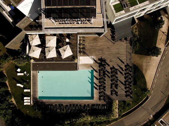 Aerial view of an outdoor pool area at a hotel with lounge chairs, umbrellas, and a rooftop deck with seating and a sign reading 'Monarch Hotel'.