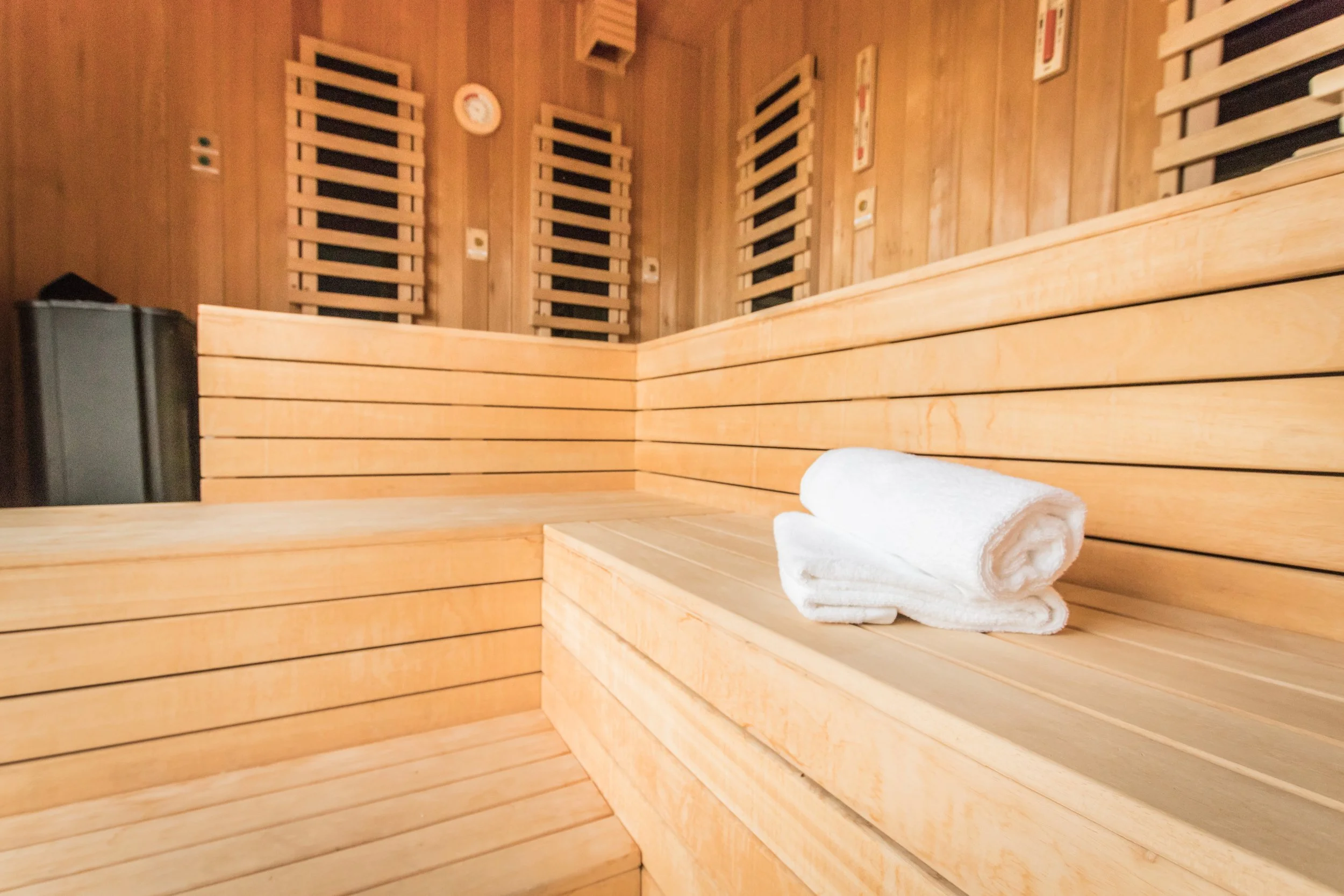 Wood-paneled sauna interior with benches, a rolled white towel, and sauna accessories on the wall.
